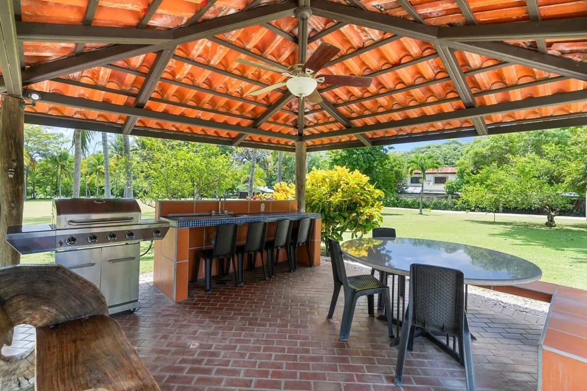 Un patio exterior cubierto tiene una parrilla, una barra con asientos y una mesa de comedor.