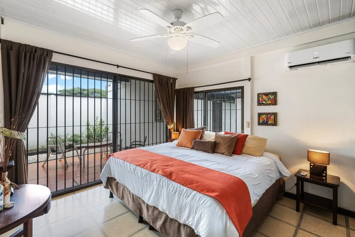 Un dormitorio con una cama, ventanas grandes y cortinas oscuras.