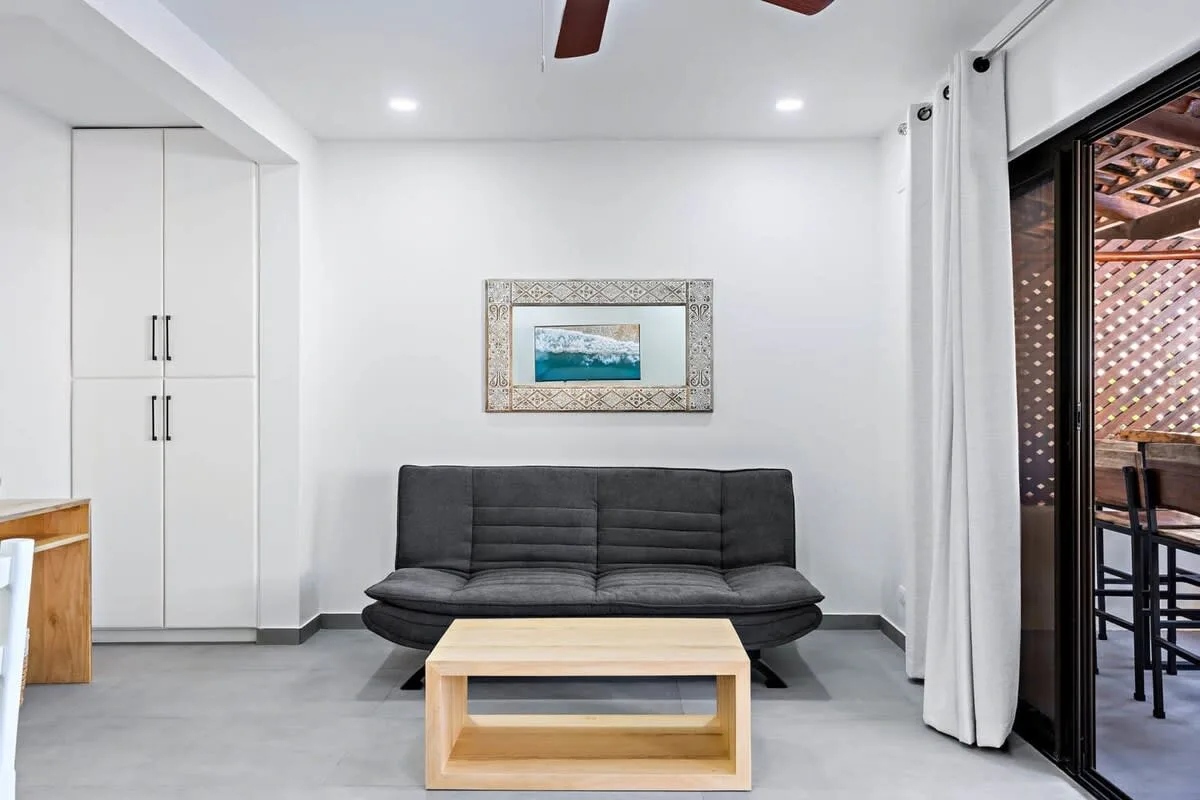 A bright living room with dark seating, a low table, and framed wall art.