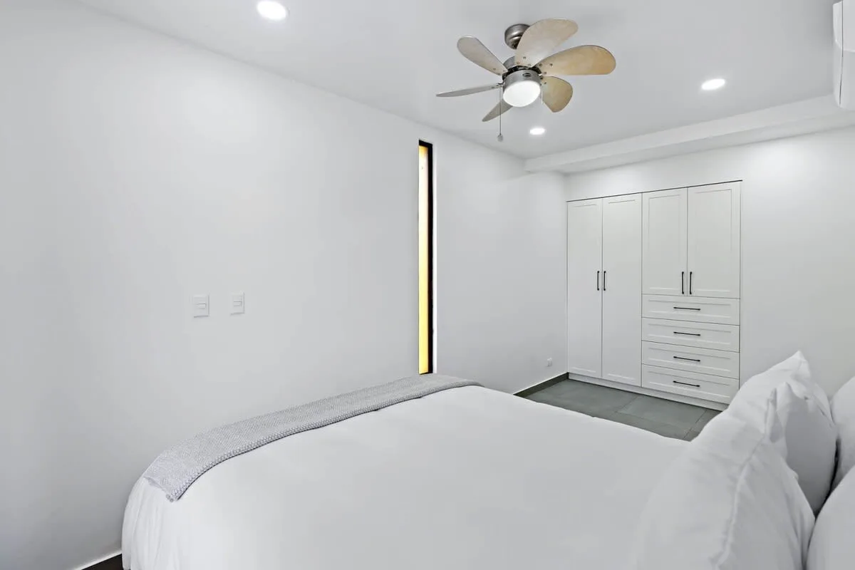 A bright bedroom with white bedding and built-in storage.