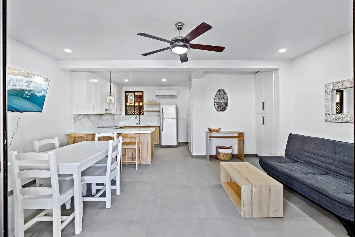 A bright open-plan living and dining area with a kitchen and dark seating.