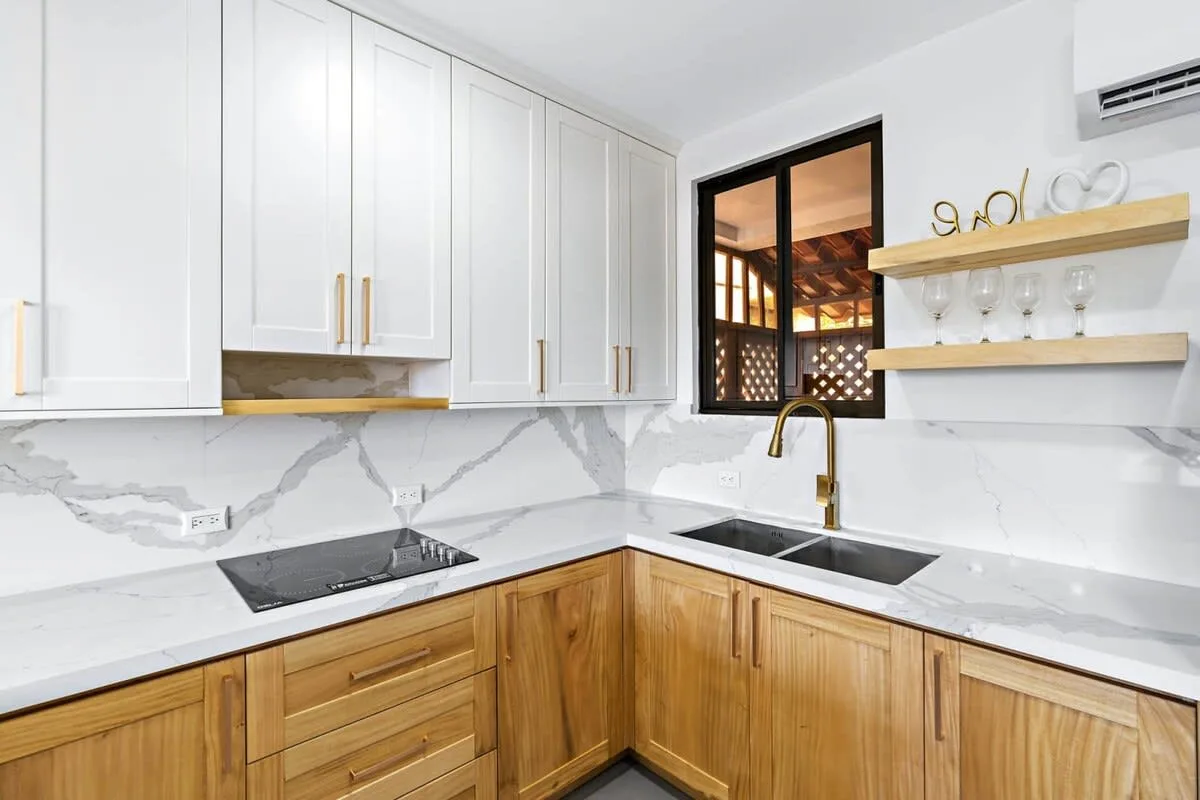 A bright kitchen with white upper cabinets, wooden lower cabinets, and a corner sink.