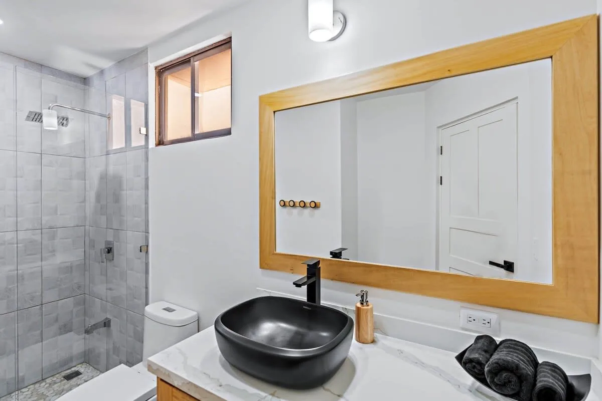 A bathroom with a glass shower, vessel sink, and large wall mirror.