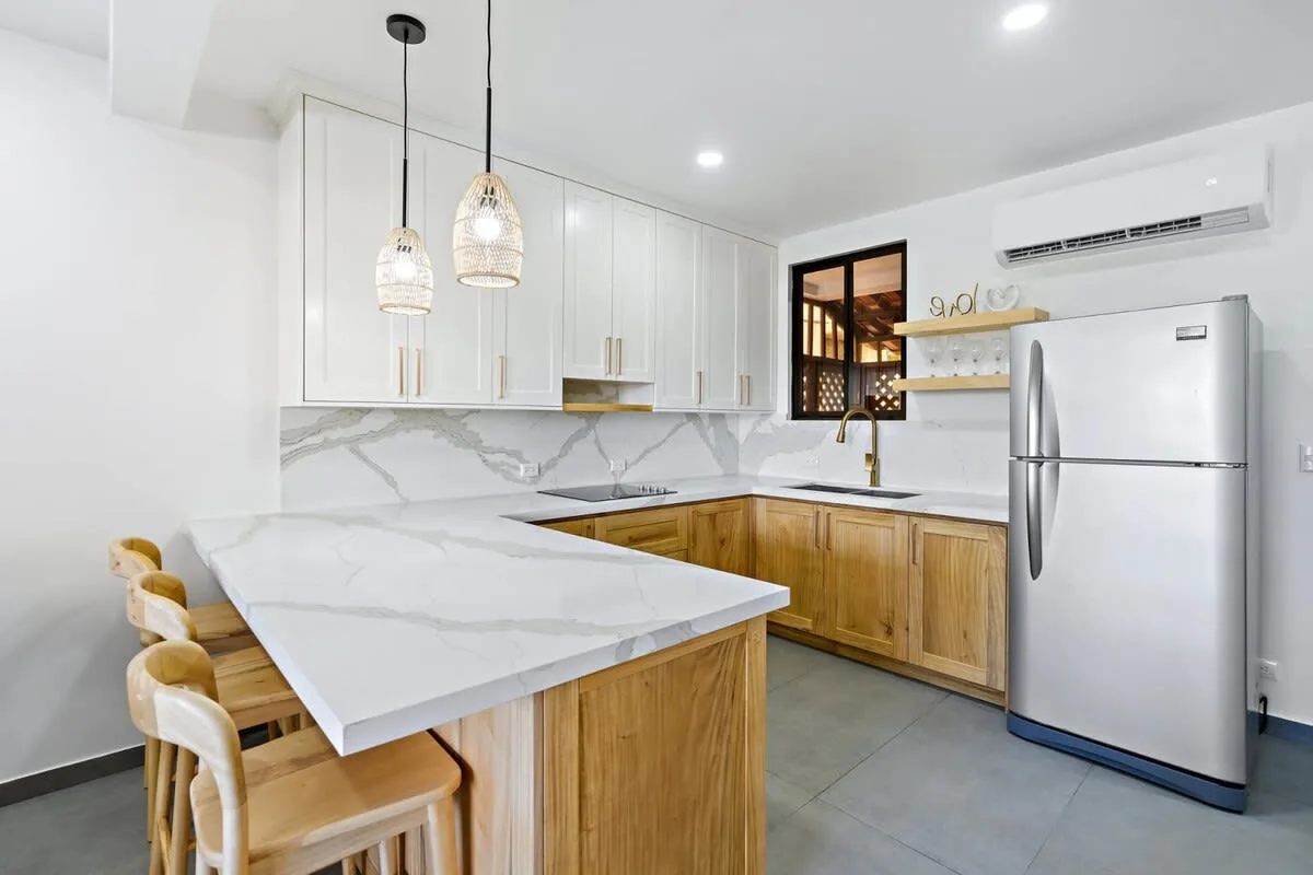A bright kitchen with a marble-patterned island and wooden cabinetry.