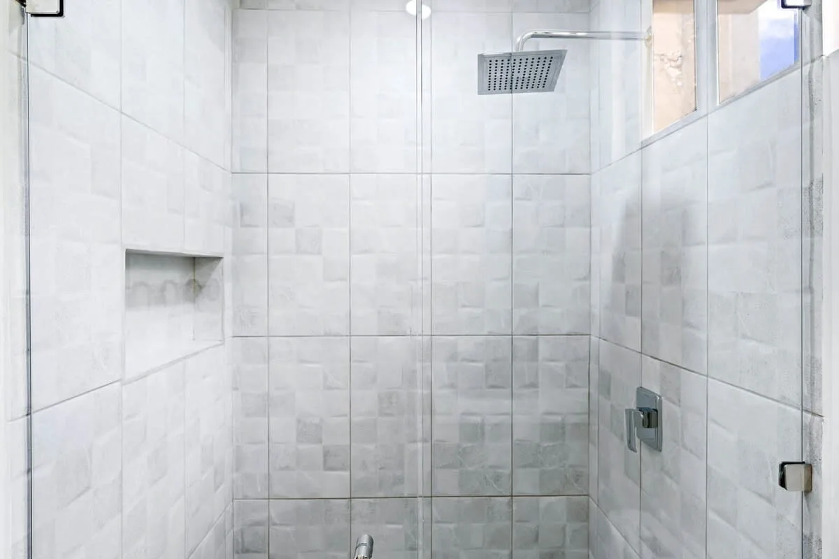 A tiled shower with a glass partition and overhead showerhead.