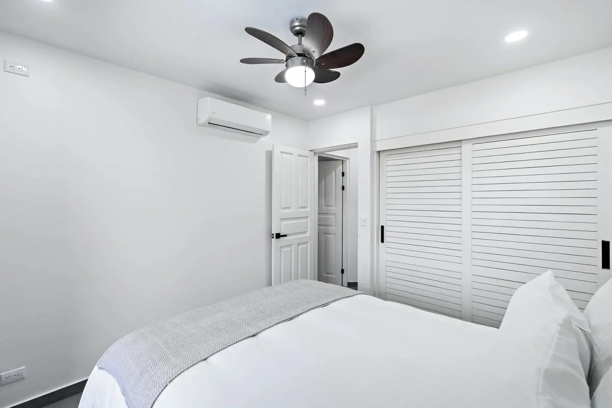 A bright bedroom with a bed and white louvered closet doors.