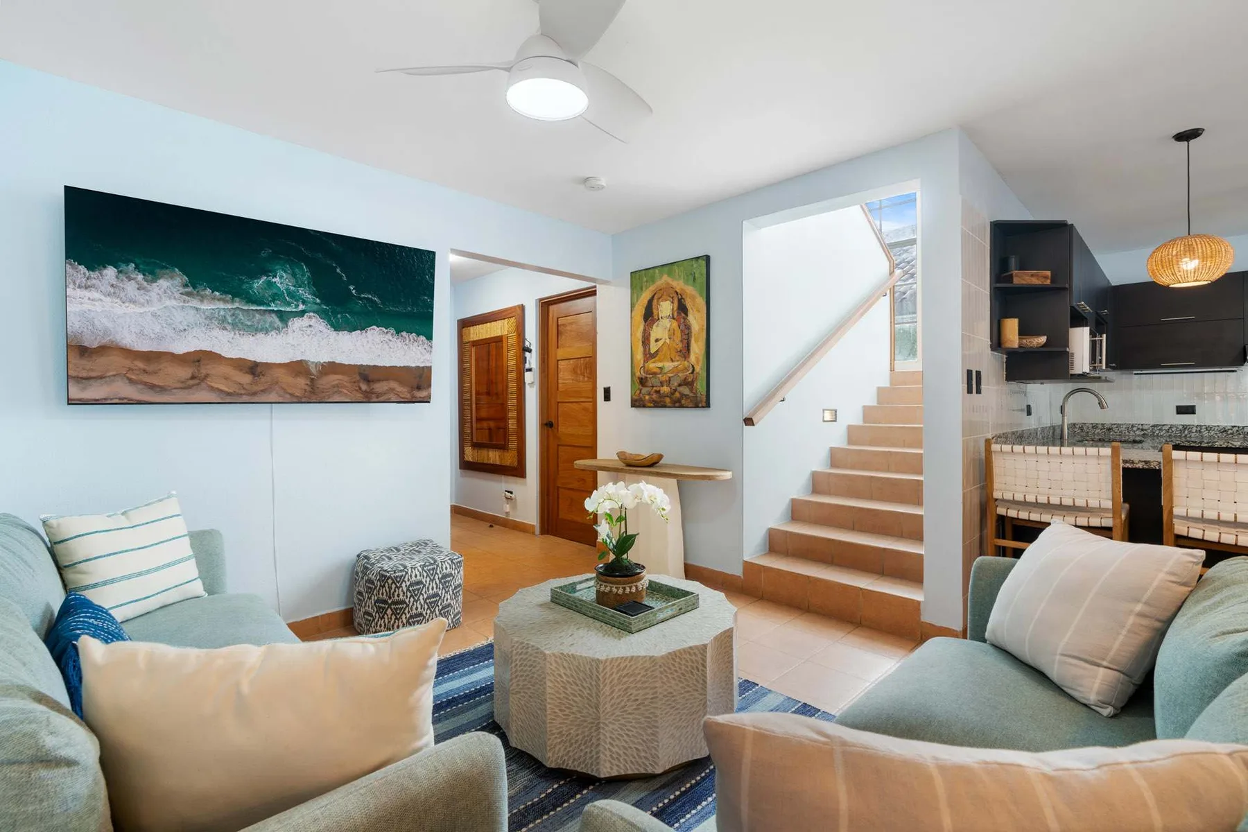 Una sala de estar con asientos y una escalera junto a una cocina abierta.