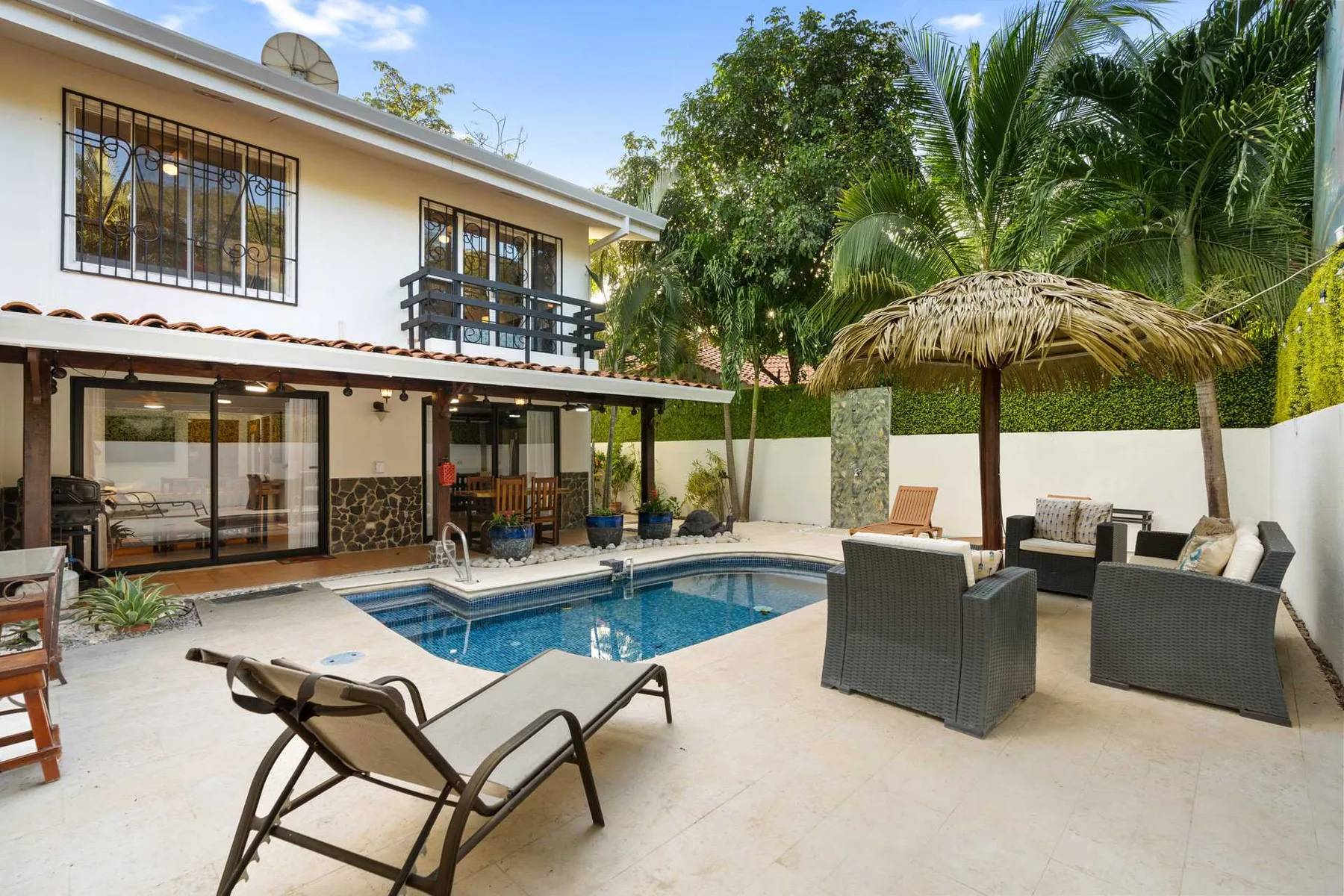 Un patio con piscina, asientos de exterior y una cubierta de paja.