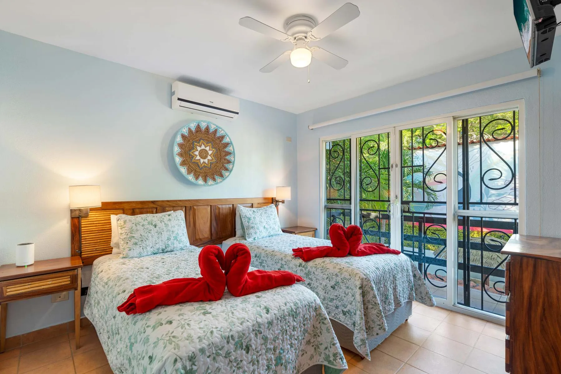 Un dormitorio con dos camas, toallas rojas decorativas y puertas de vidrio hacia un balcón.