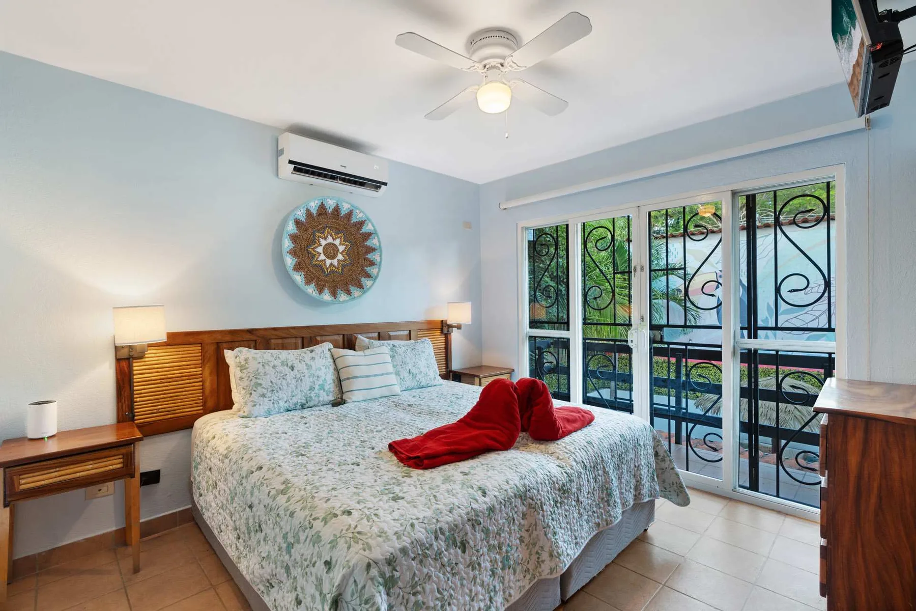 Un dormitorio con una cama bien tendida y grandes ventanas con rejas decorativas.