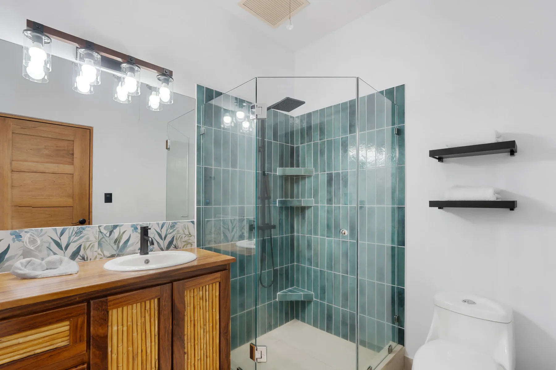 Un baño con un mueble de madera, lavabo y ducha con mampara de vidrio.