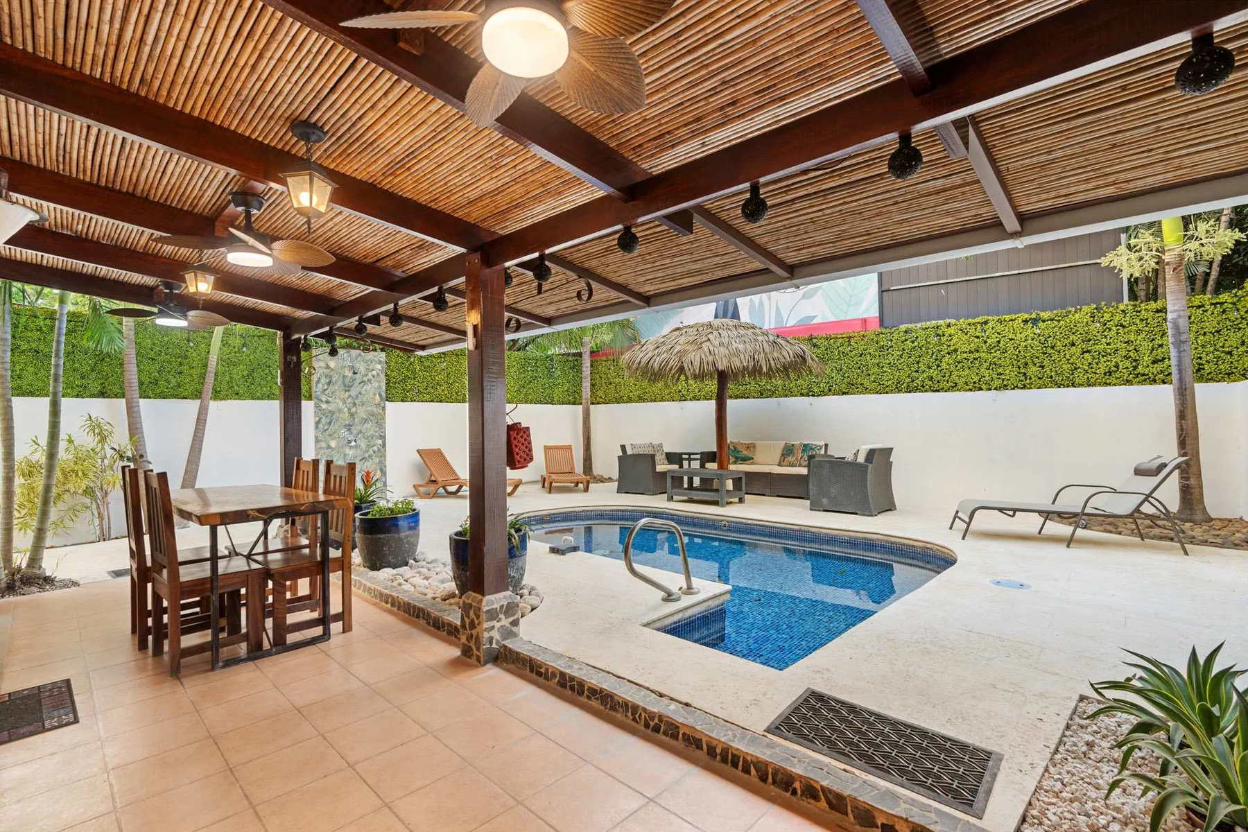 Un patio cubierto da a una pequeña piscina, con asientos al aire libre cerca.