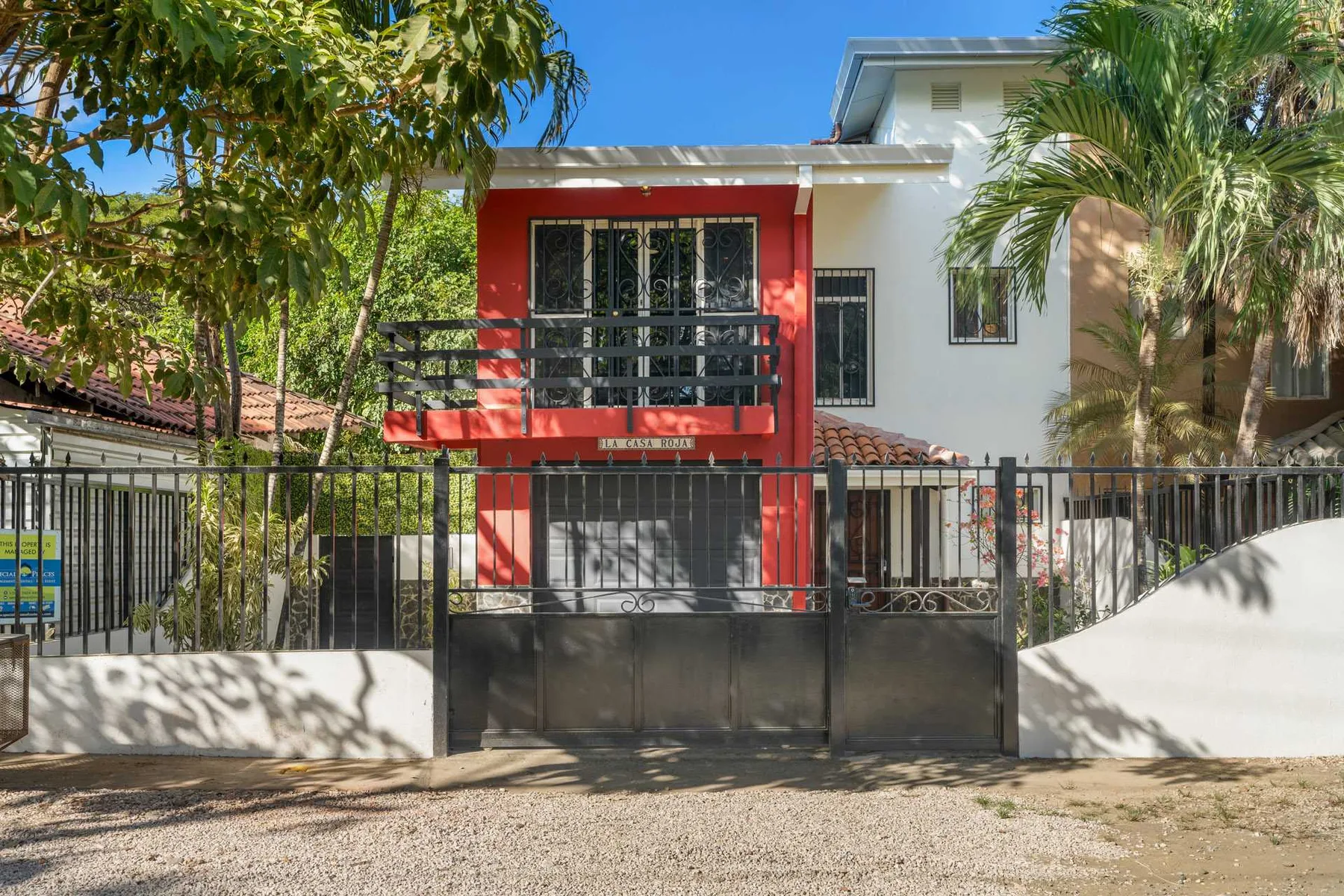 Una casa de dos pisos con un balcón rojo se encuentra detrás de una reja negra.