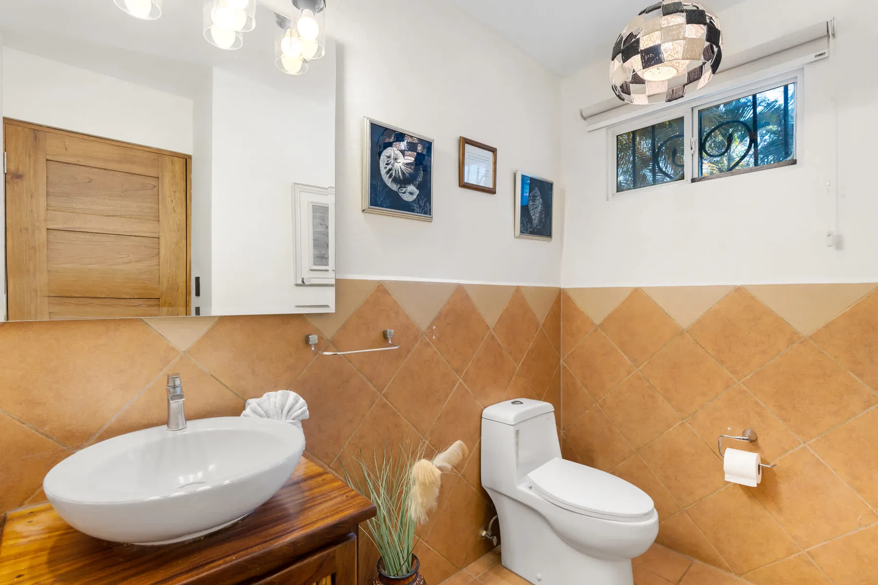 Un baño con lavabo sobre encimera, inodoro y paredes de azulejos color tostado.
