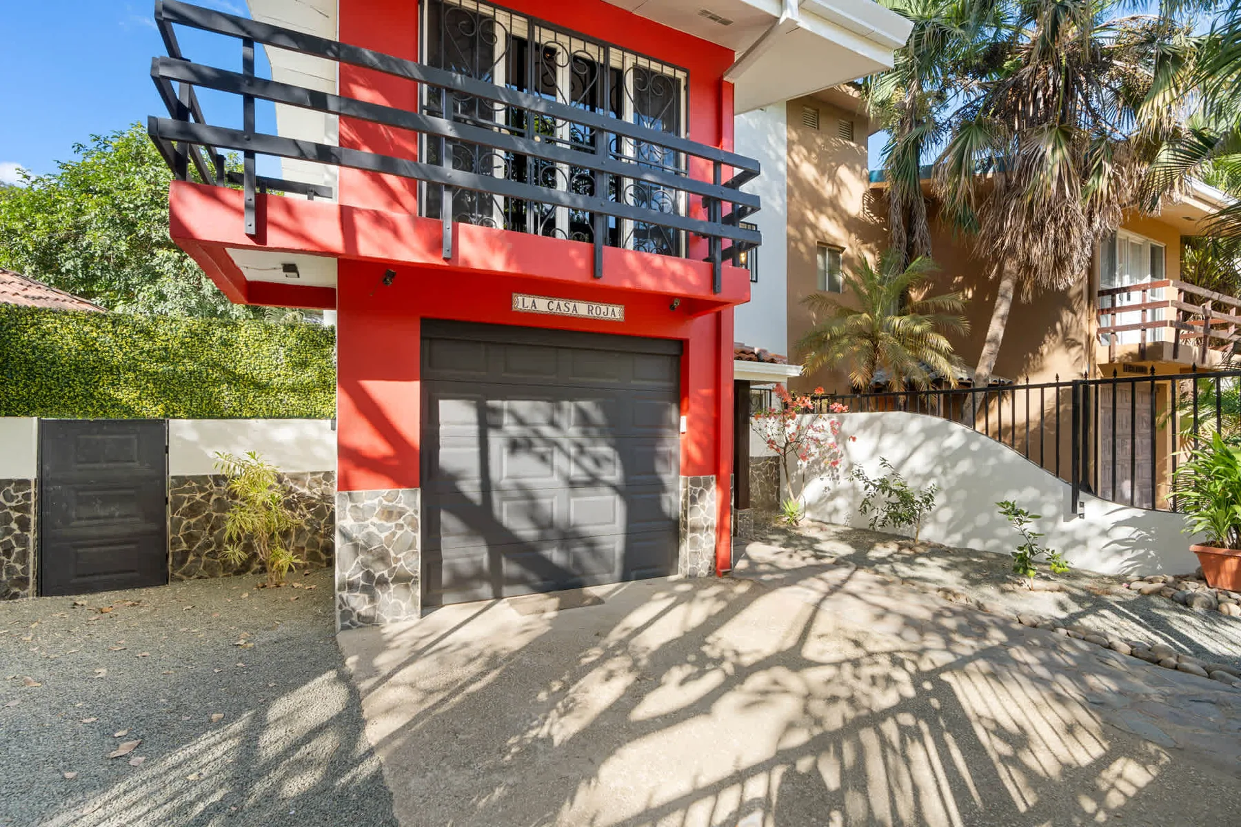 Entrada de un edificio rojo con una puerta de garaje oscura y un balcón encima.