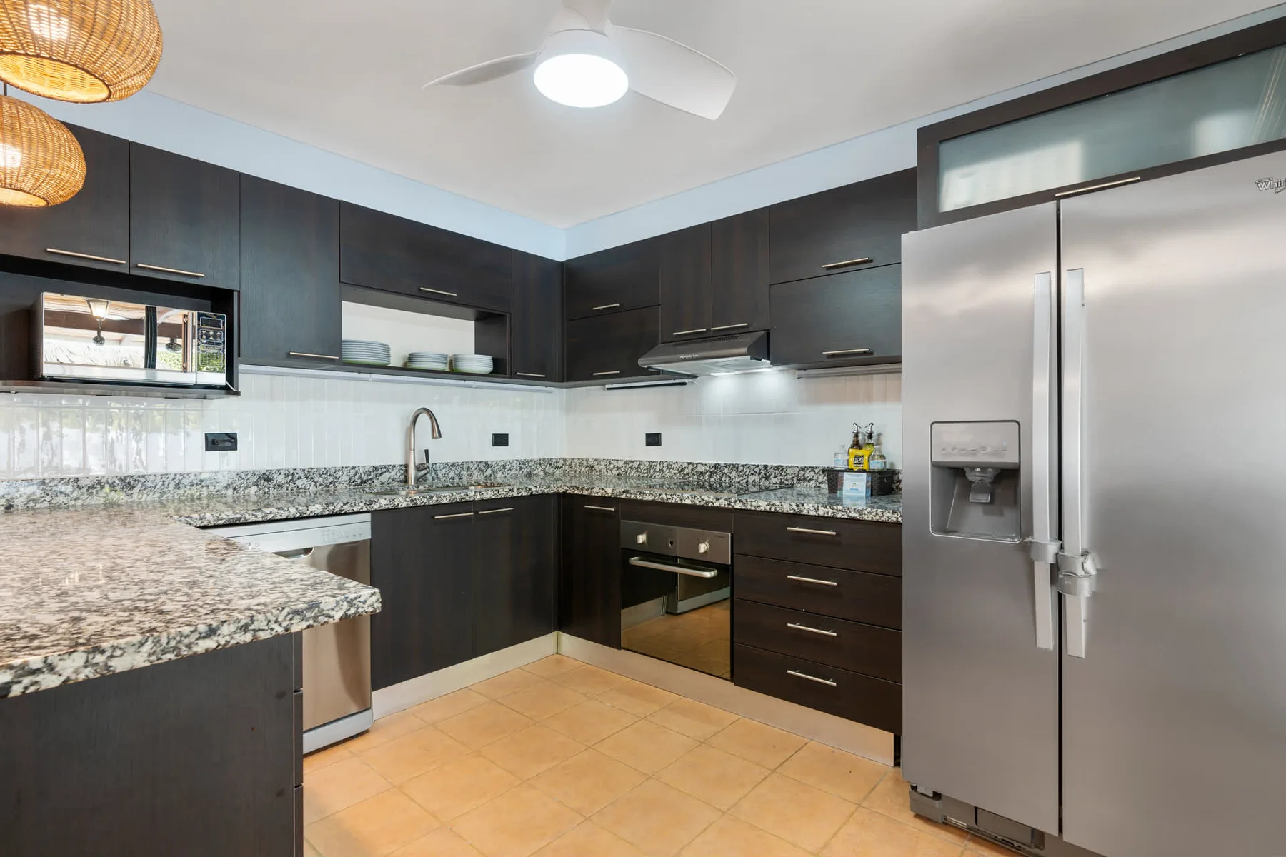 A modern kitchen with dark cabinets, granite countertops, and stainless steel appliances.