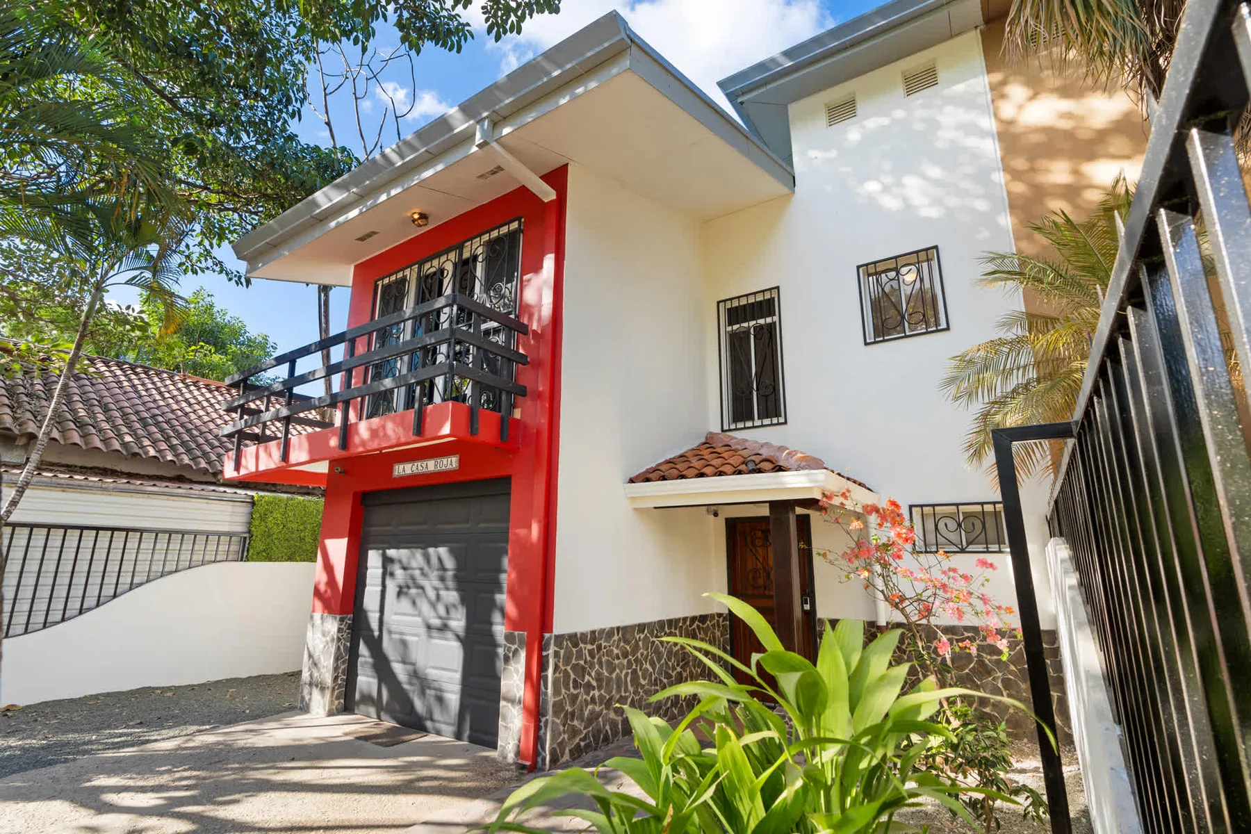 Una casa de dos pisos con balcón rojo se encuentra junto a una entrada pavimentada.