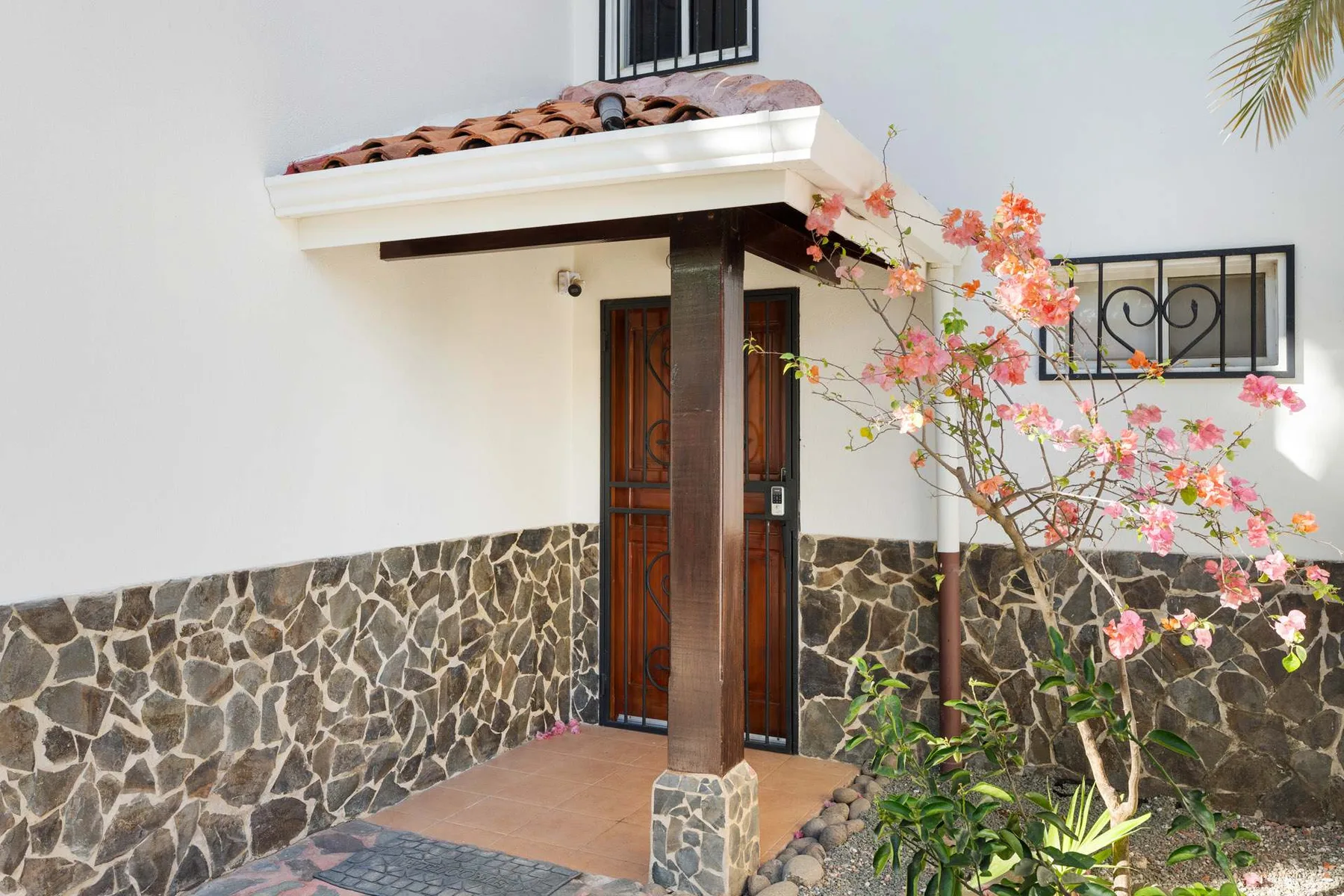 La entrada exterior tiene un alero de tejas, piedra y plantas con flores.
