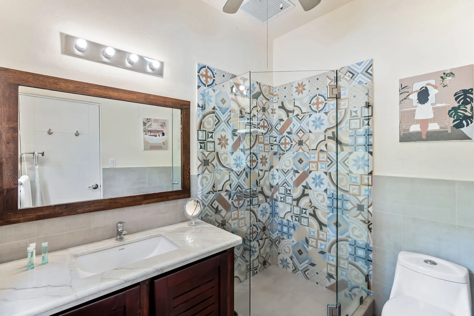 A bathroom with a sink, large mirror, and patterned tile shower area.