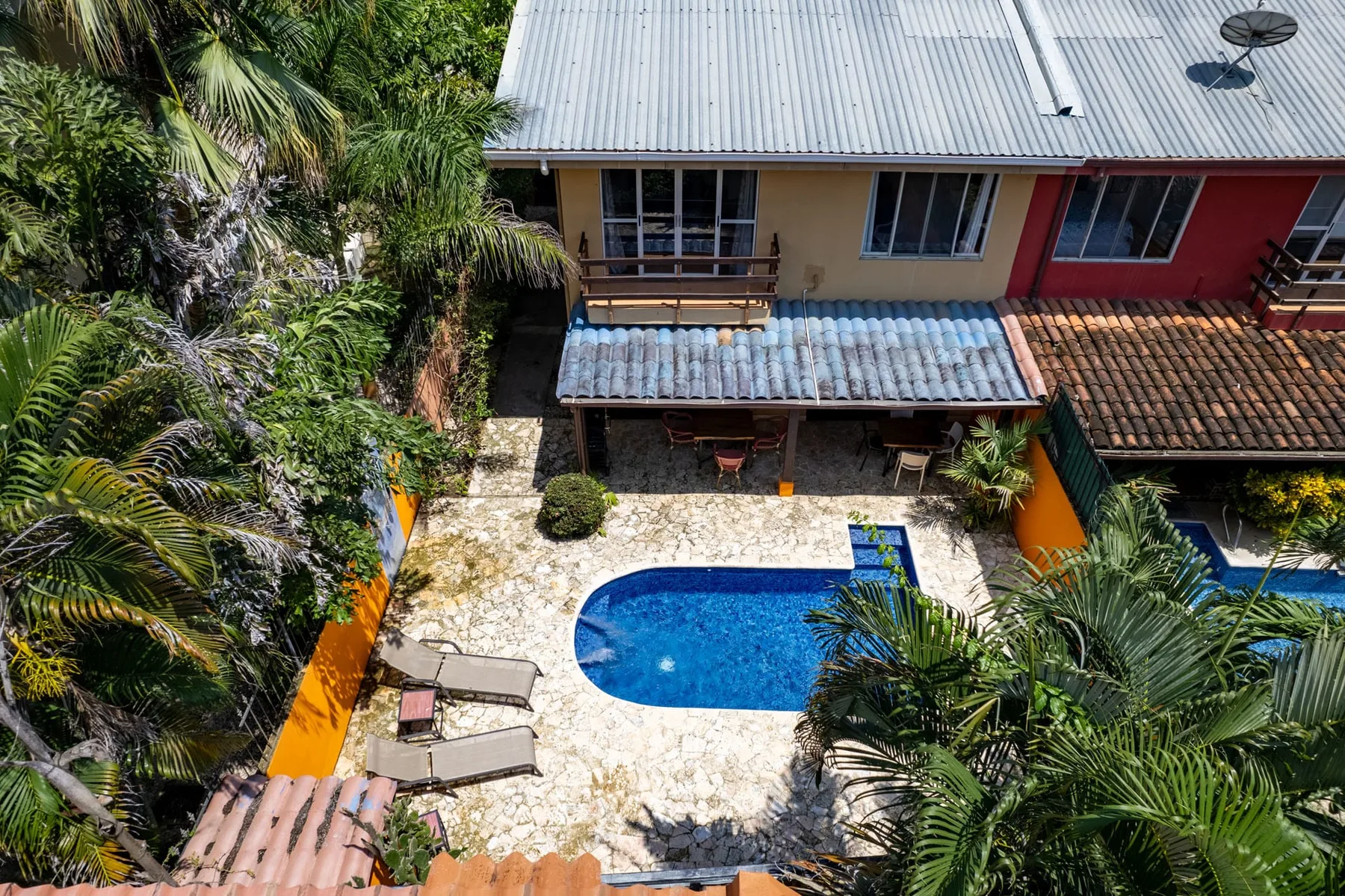 An aerial view shows a blue swimming pool beside a tiled patio and tropical greenery.