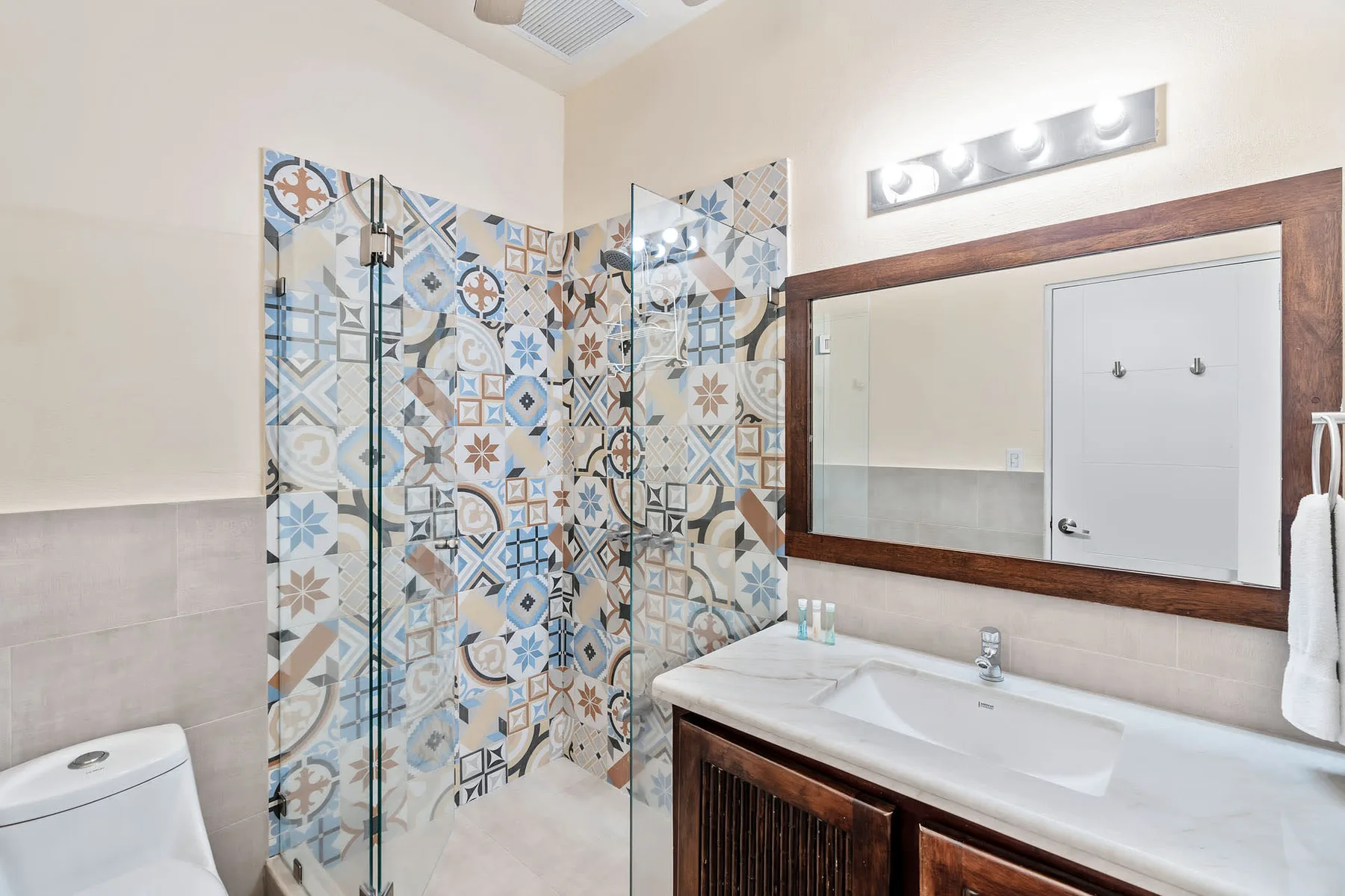 A bathroom with a patterned tile shower, sink, and wide wall mirror.