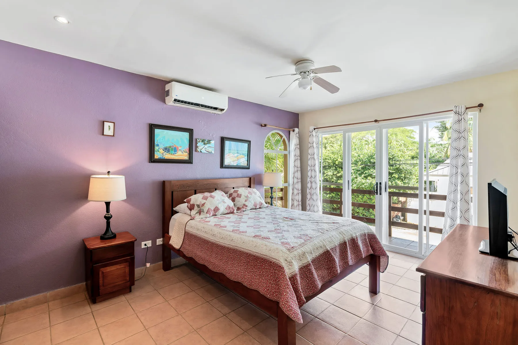 A bedroom with a bed, bedside table, and large windows overlooking greenery.