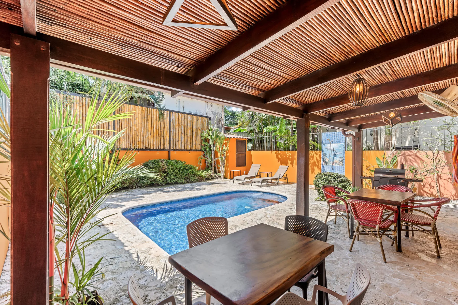 A covered patio overlooks a swimming pool, with outdoor tables and seating.