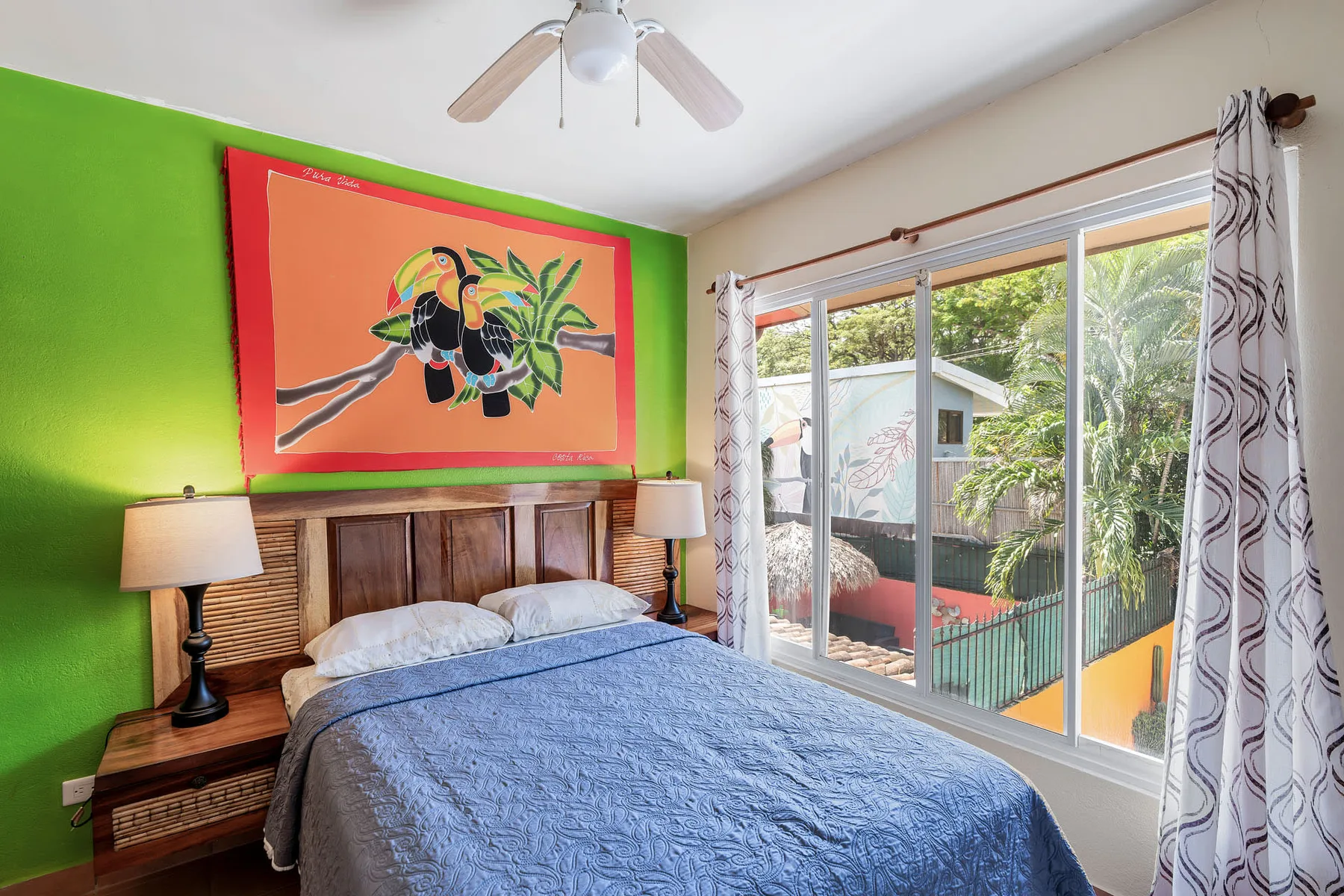 A bedroom with a bed beneath colorful wall art and sliding glass doors.