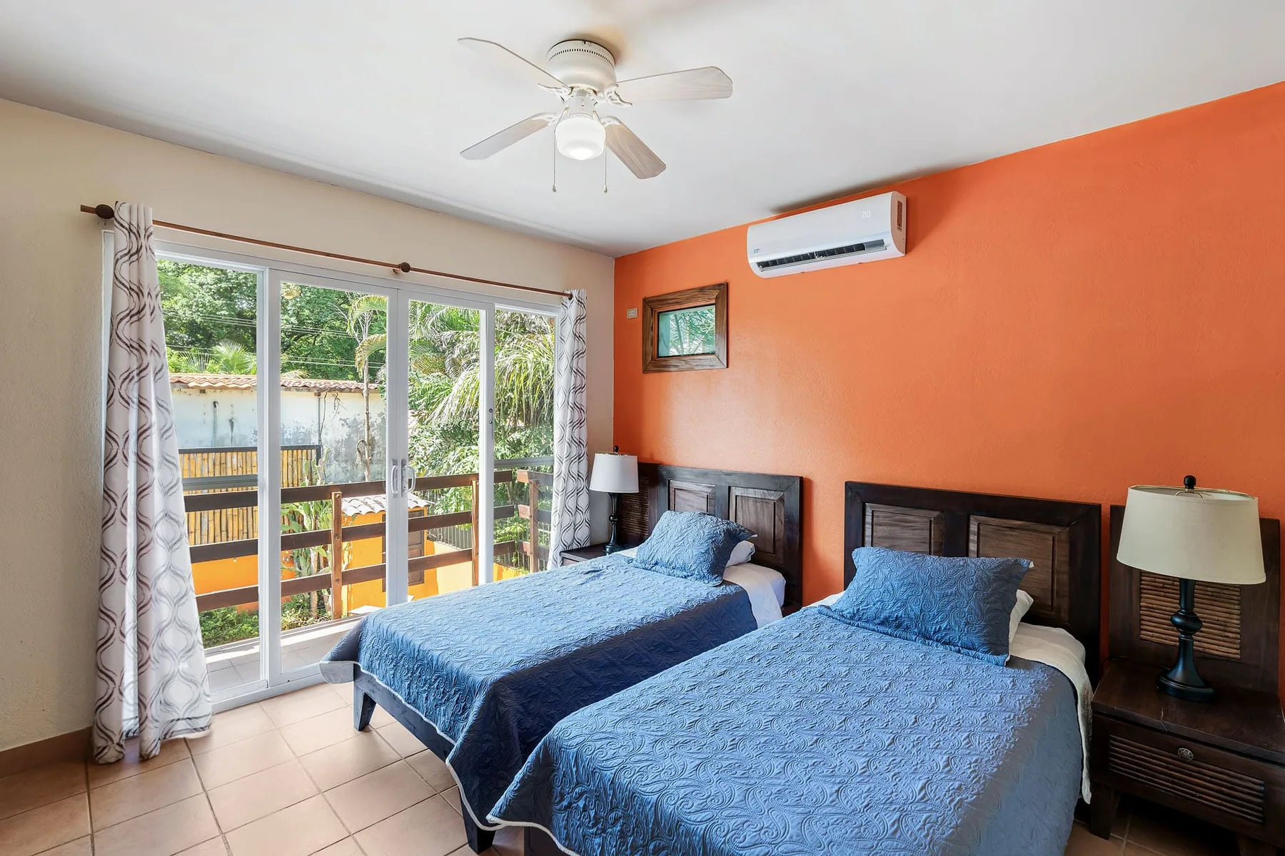 A bedroom with two beds covered in blue bedding beside large windows.