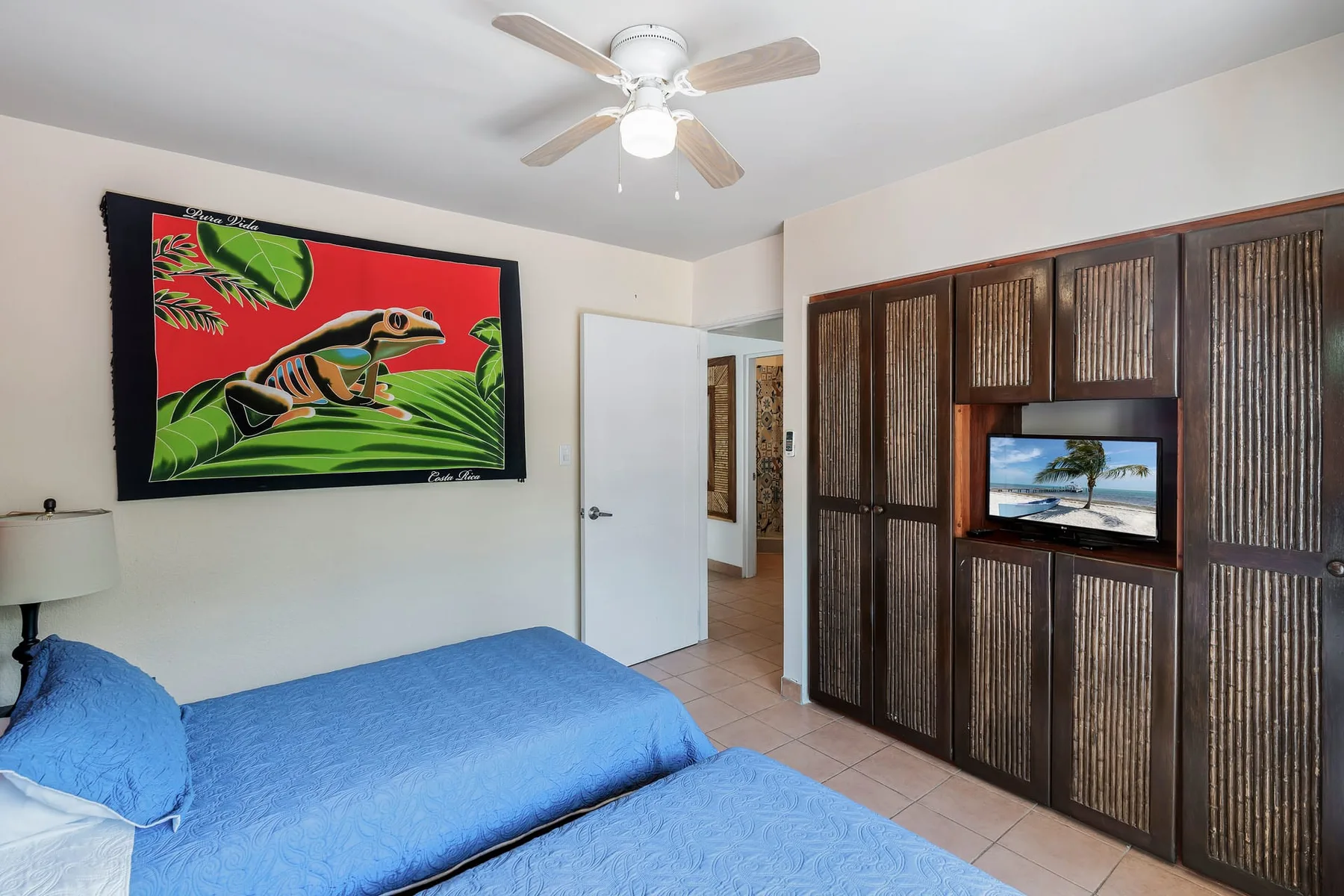 A bedroom with blue bedding, colorful wall art, and dark built-in cabinets.