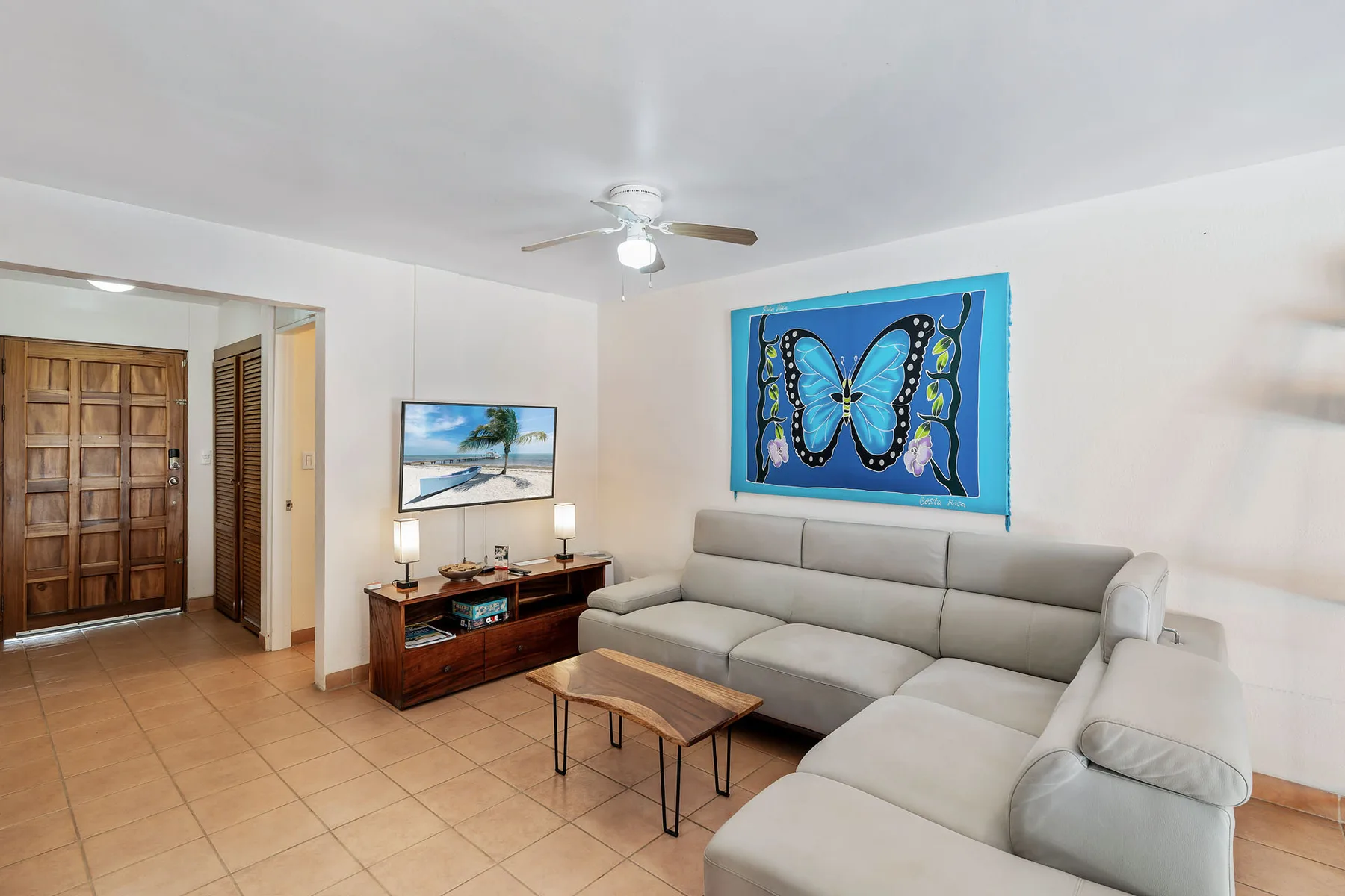 A living room with gray seating, a coffee table, and colorful butterfly artwork.