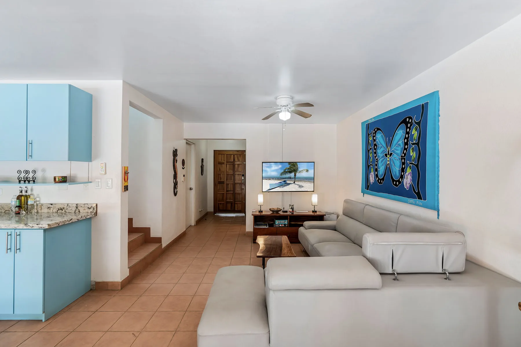 A bright living room with seating, a coffee table, and a blue butterfly wall hanging.