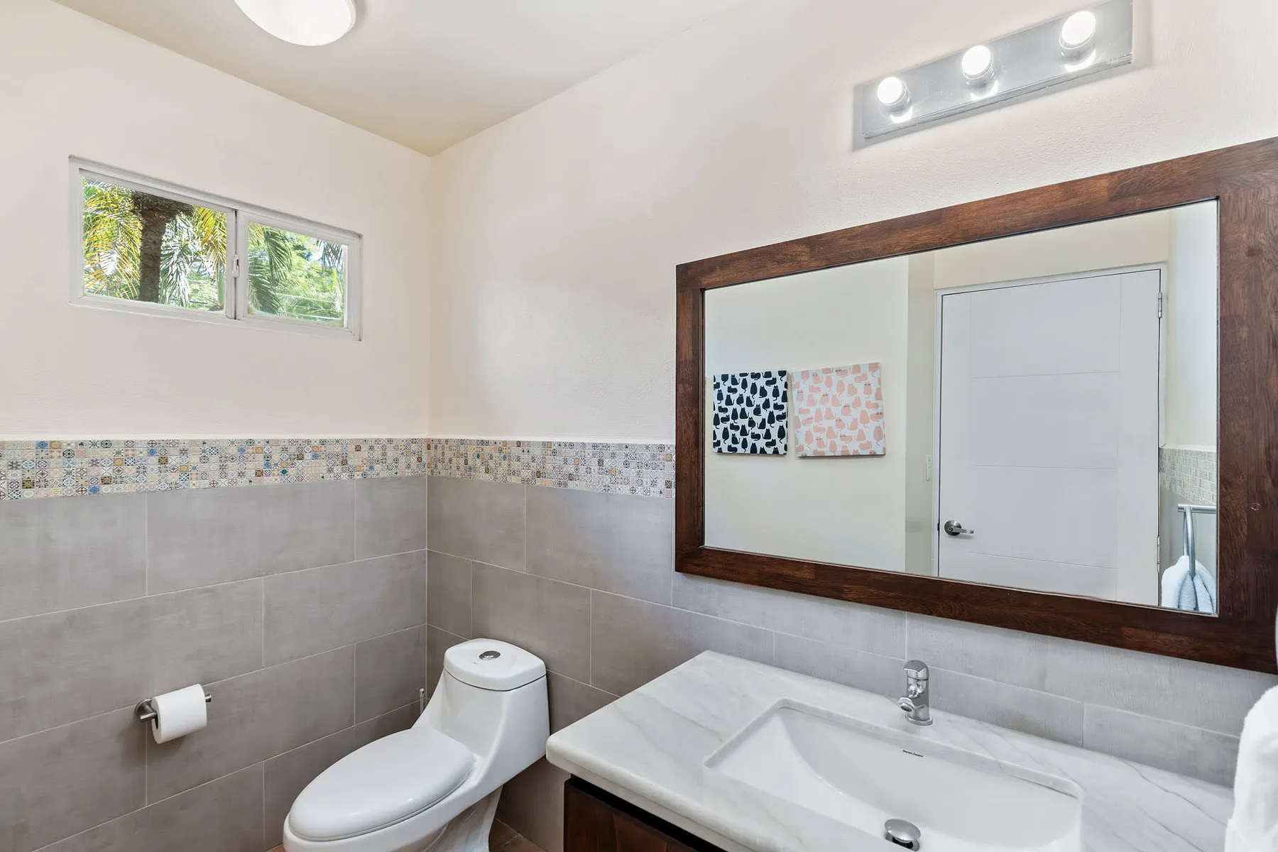 A tiled bathroom with a toilet, sink, and large wall mirror.