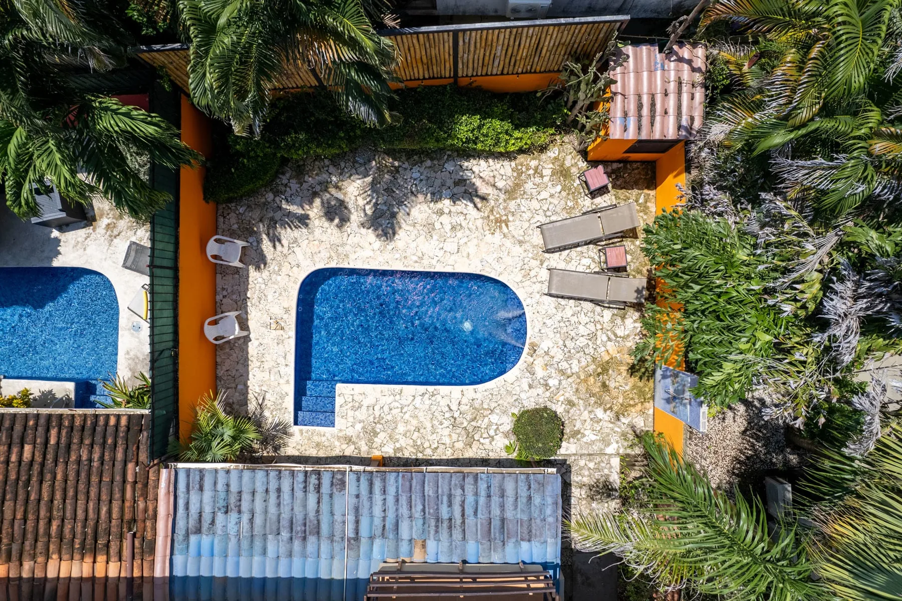An aerial view of a blue swimming pool surrounded by a stone patio and palm trees.