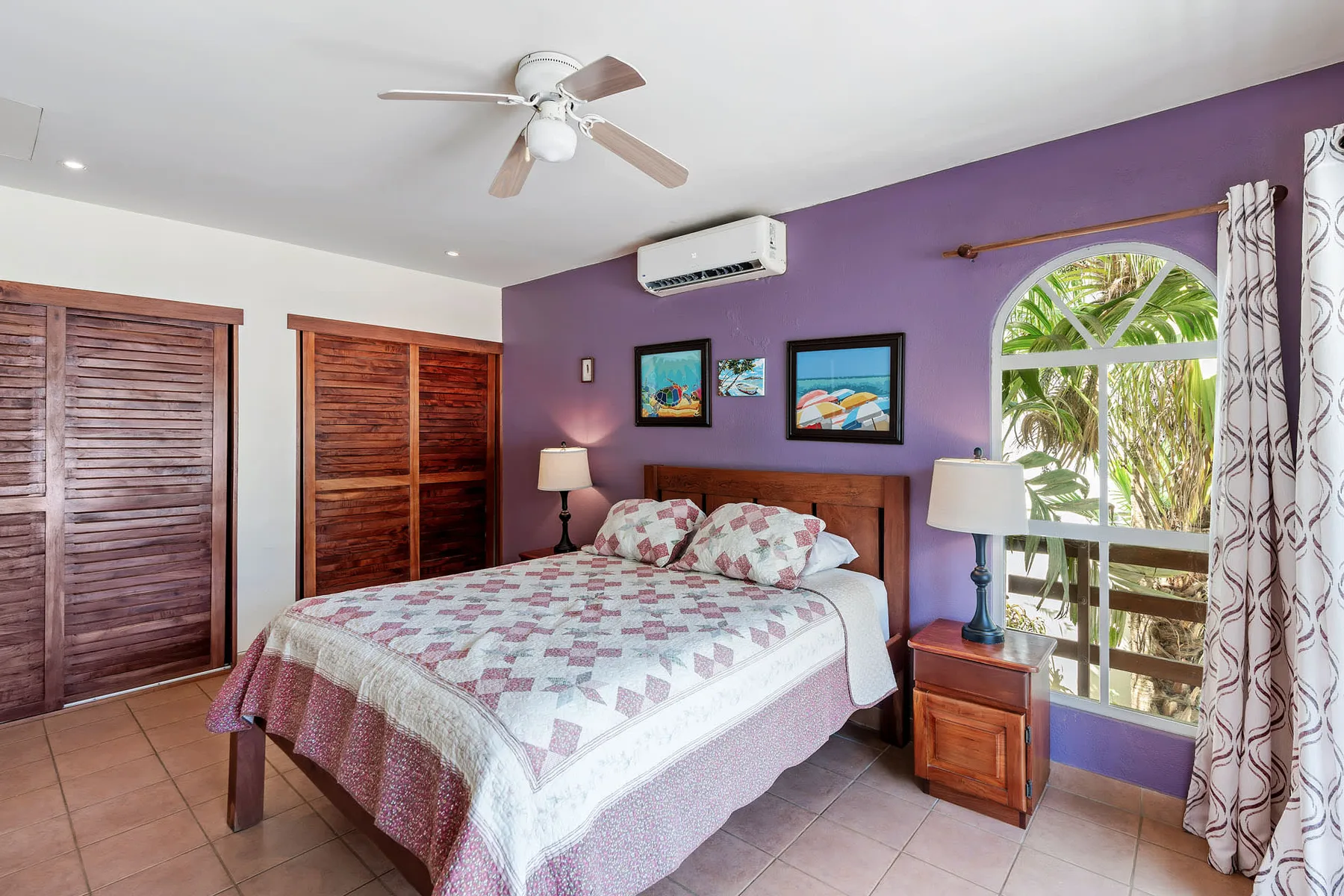 A bedroom with a bed, wooden closets, and a large arched window.