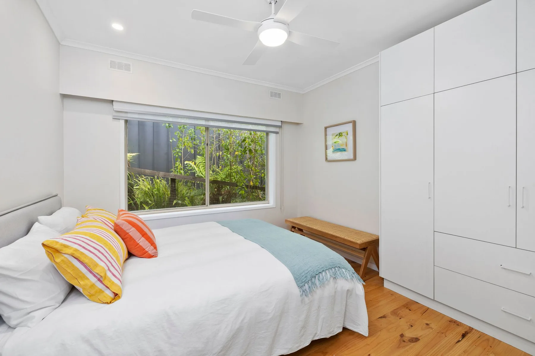 Un dormitorio luminoso con una cama, cojines coloridos y una ventana amplia.