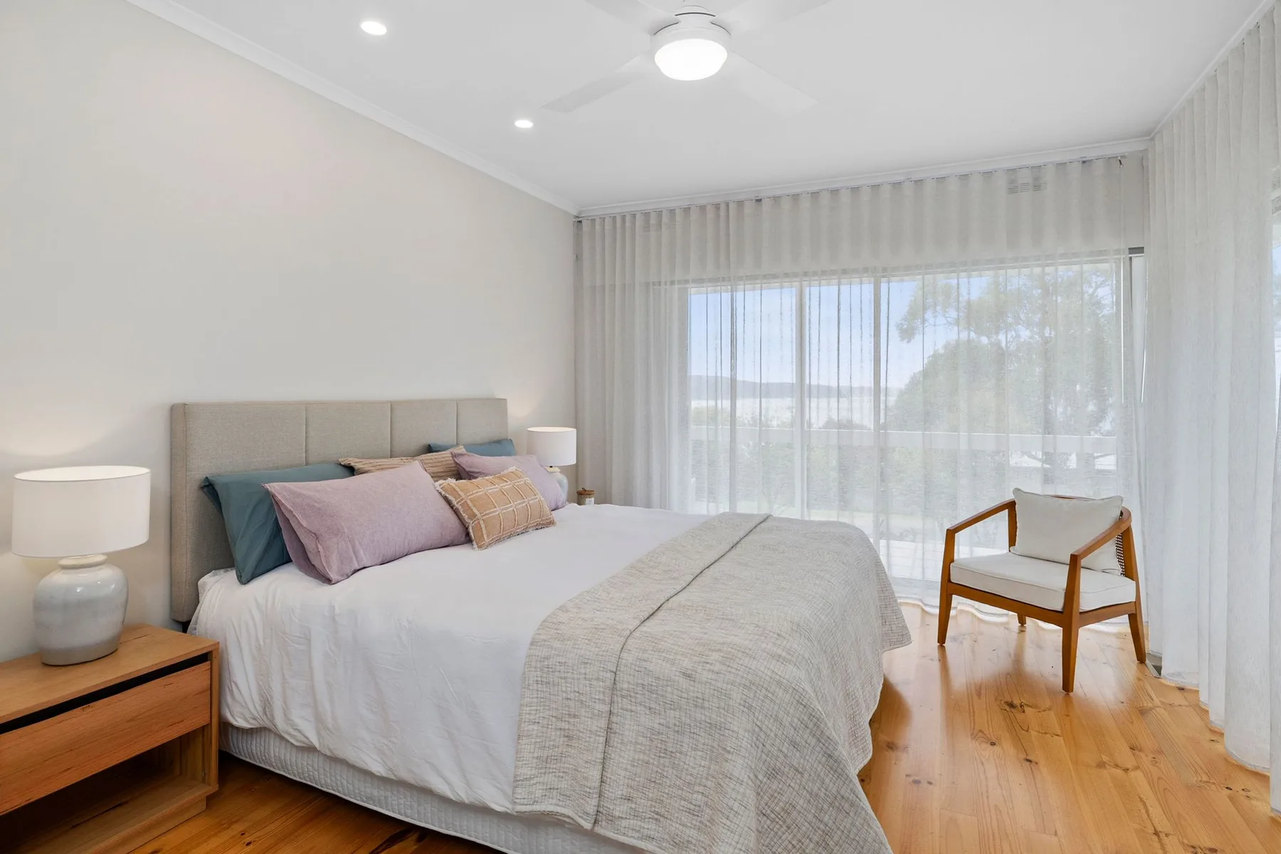 Un dormitorio luminoso con una cama junto a una gran ventana con cortinas.