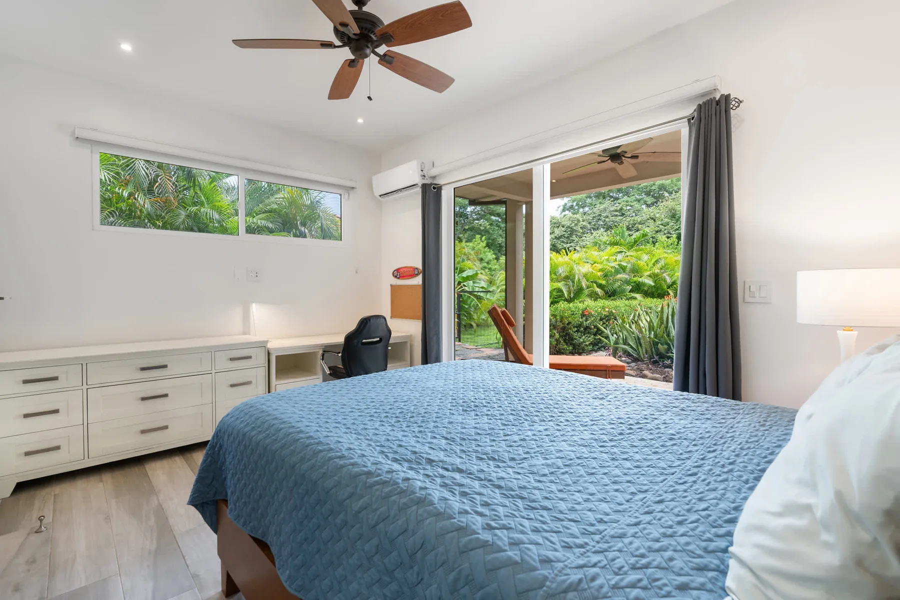 Un dormitorio luminoso con una colcha azul y puertas corredizas de vidrio hacia la vegetación.