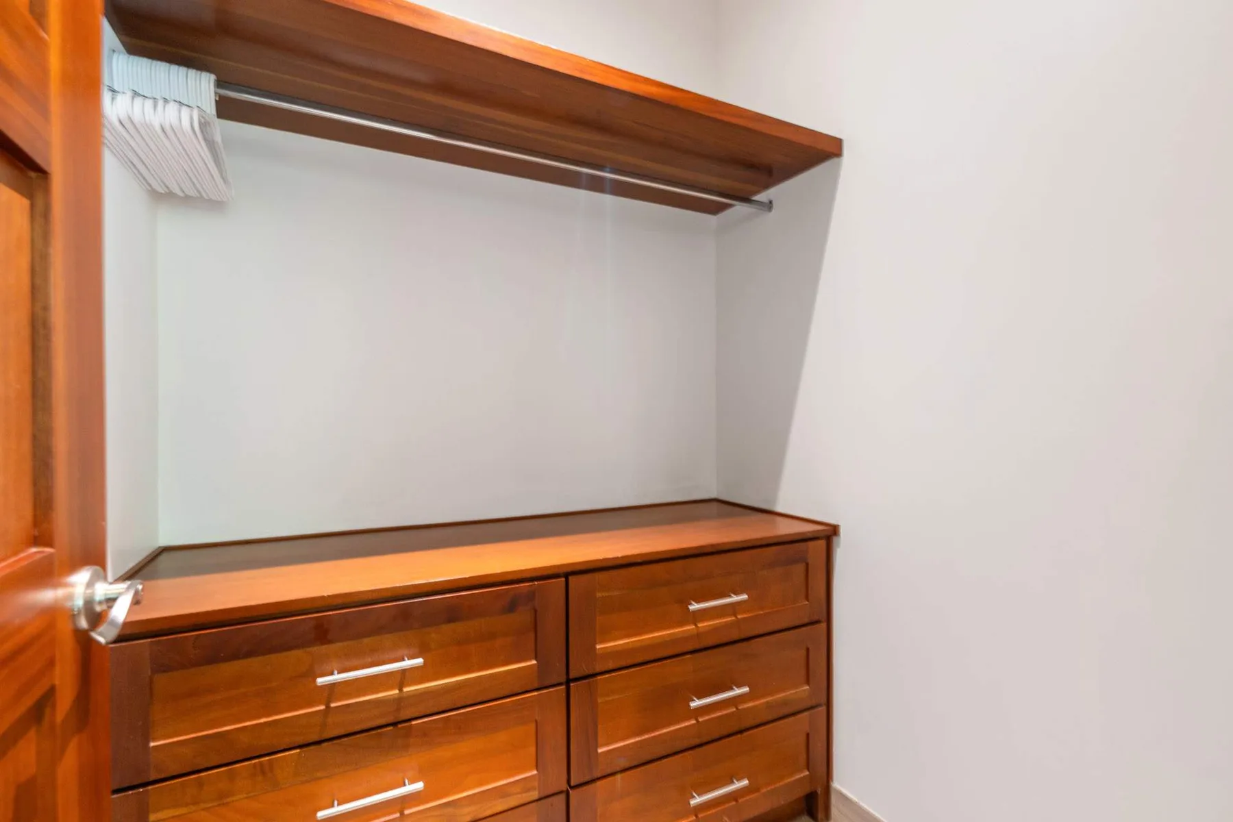 Un área de armario en un dormitorio con un mueble de madera y un estante superior.