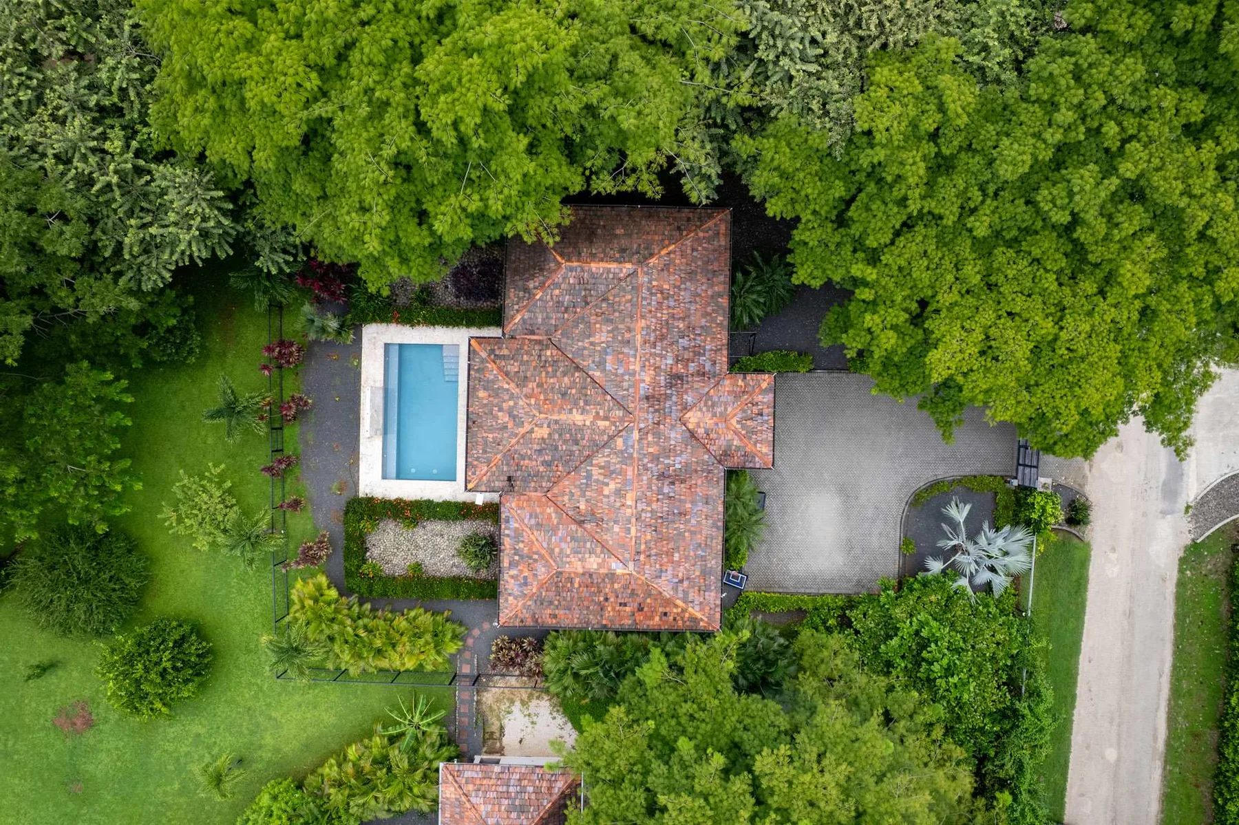 Vista aérea de una casa con techo de tejas rodeada de árboles, con una piscina al lado.