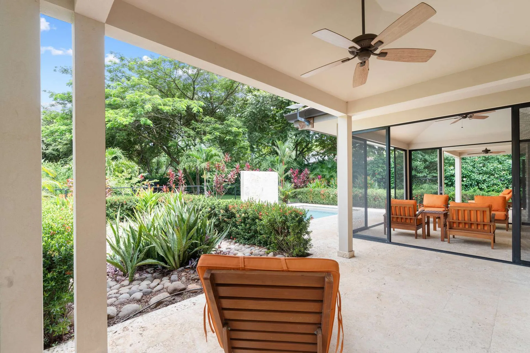 Un patio cubierto con asientos da a un jardín y una piscina.