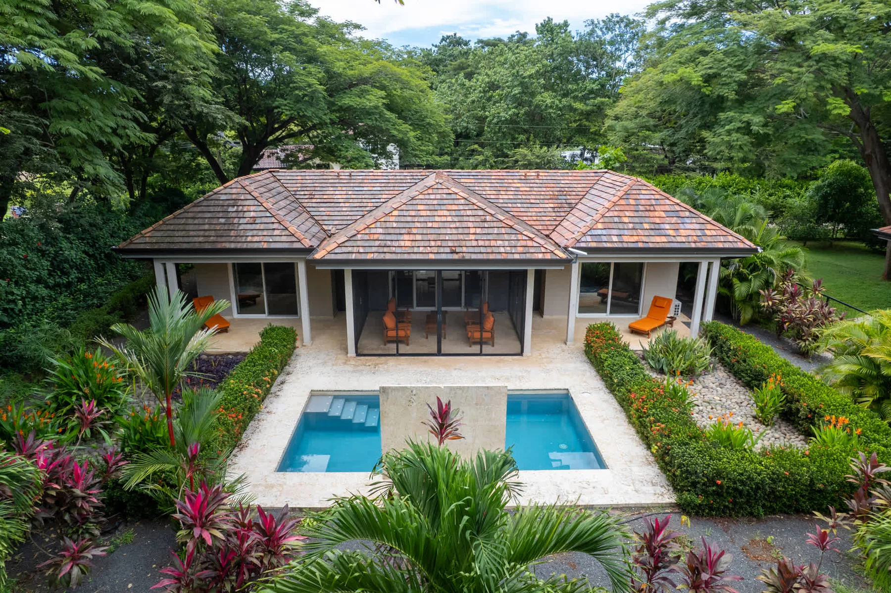 Un patio ajardinado con una piscina rectangular frente a un pabellón de techo de tejas.