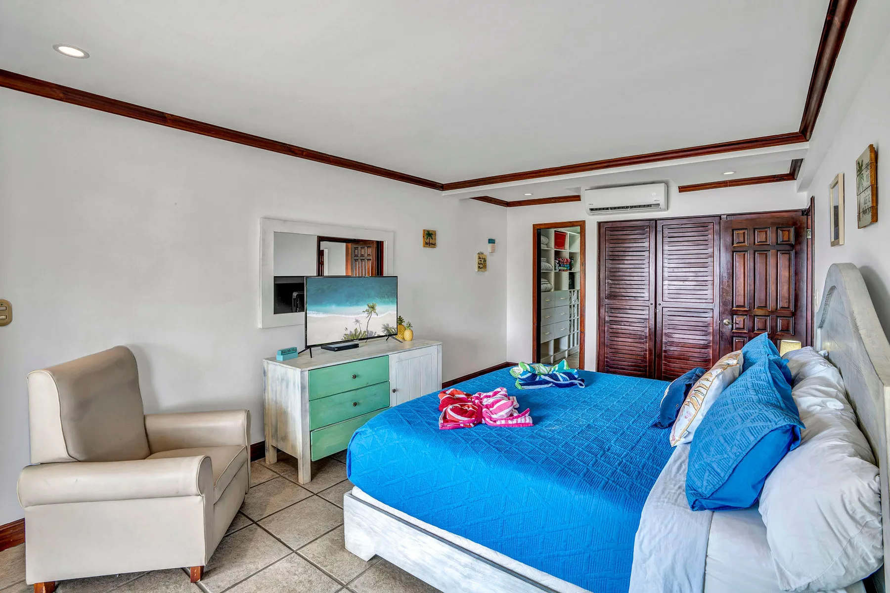 A bedroom with a blue bed, an armchair, and a television on a dresser.