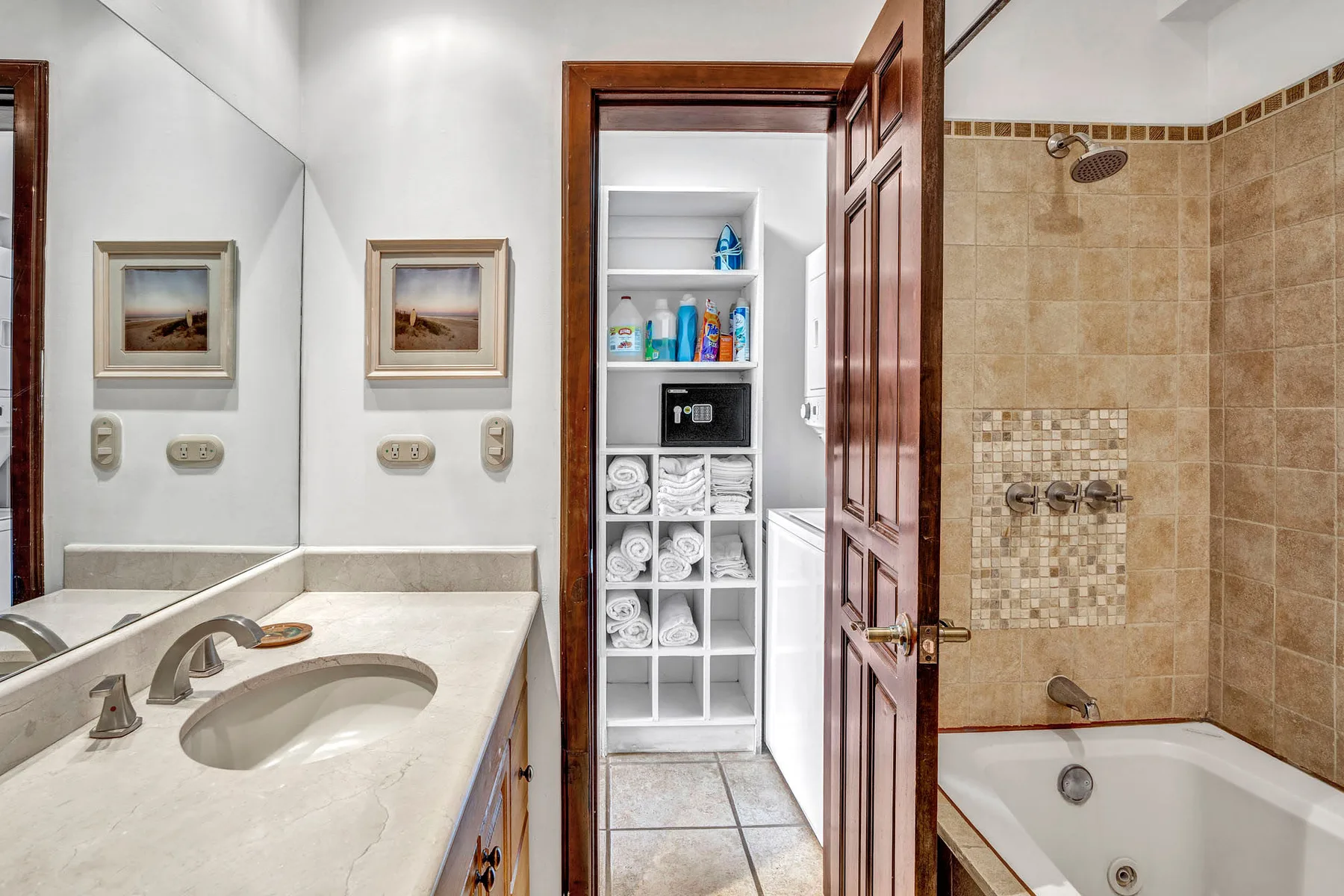 A bathroom with a sink vanity, bathtub, and open doorway to a linen shelf.