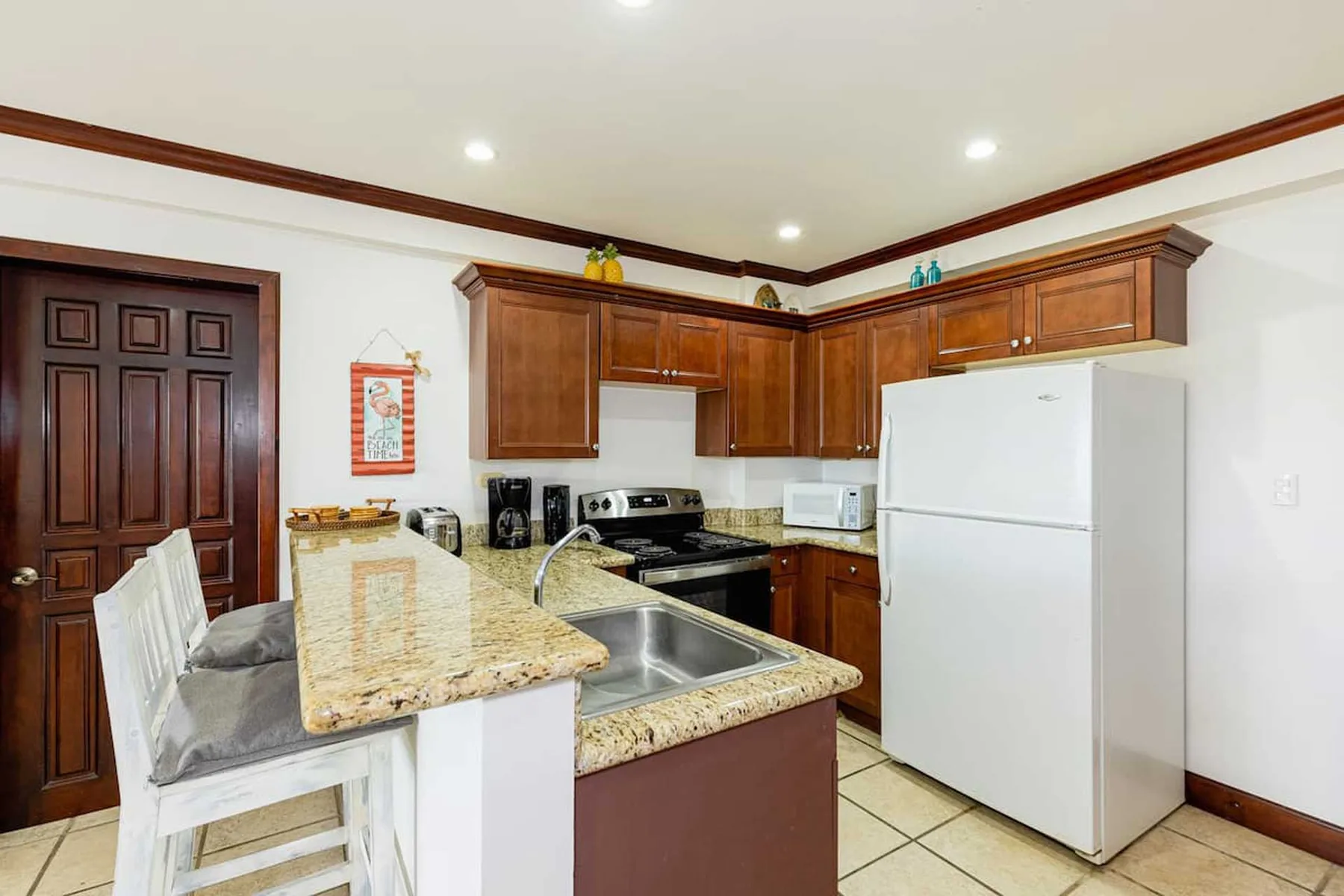 A kitchen with wooden cabinets, a refrigerator, and a granite countertop.