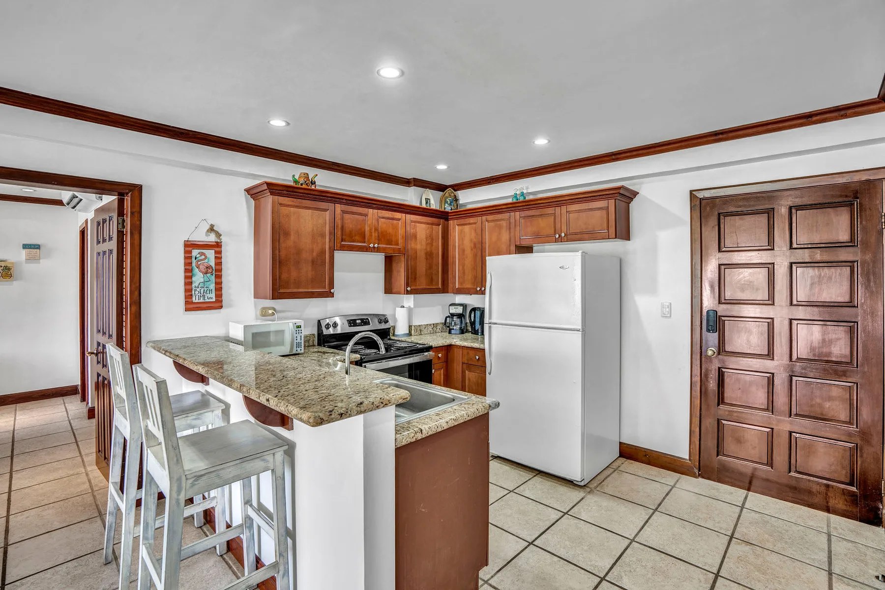 A kitchen with wooden cabinets, a refrigerator, and a breakfast counter.