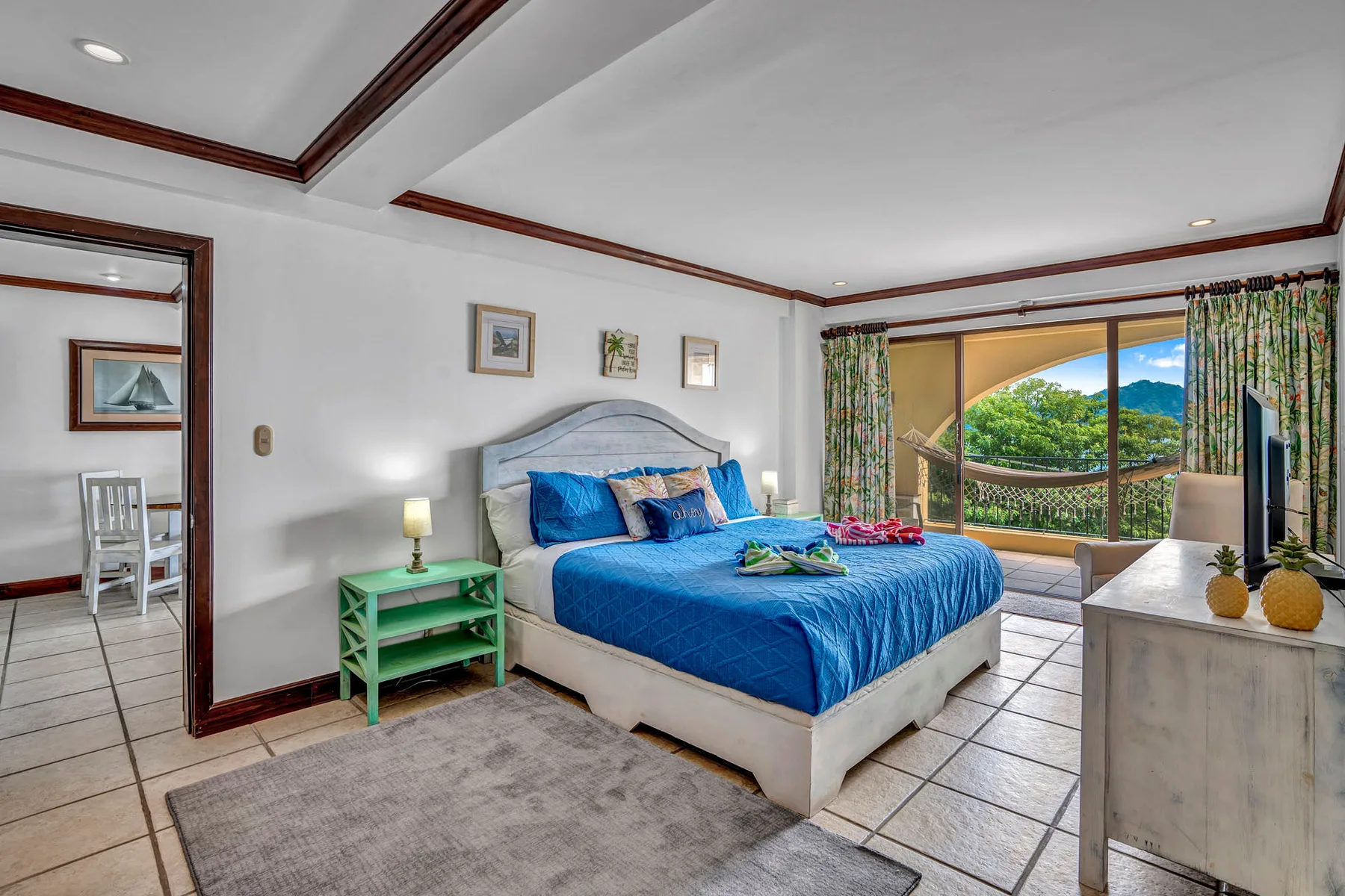A bedroom with a blue-covered bed beside a large window overlooking green hills.