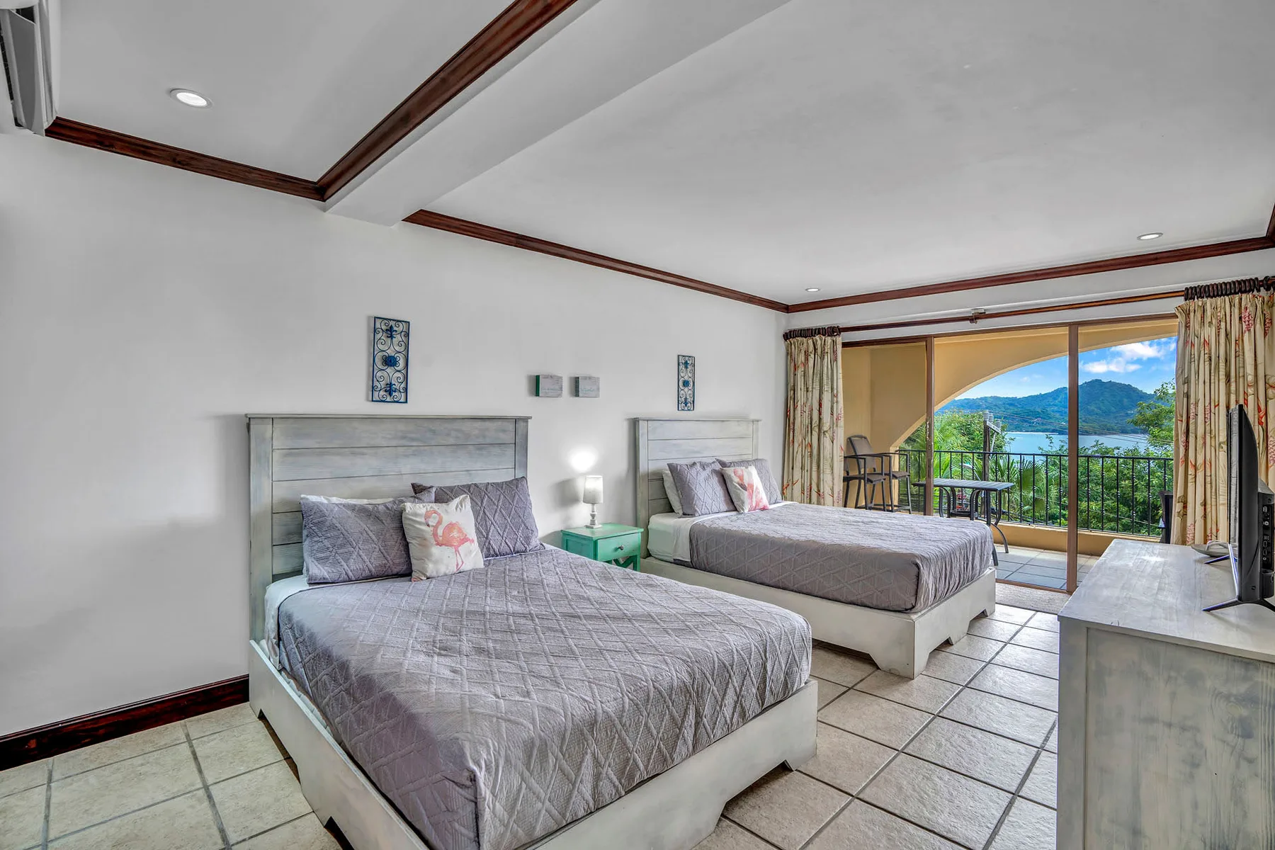 A bedroom with two beds, a tiled floor, and glass doors opening to a balcony.