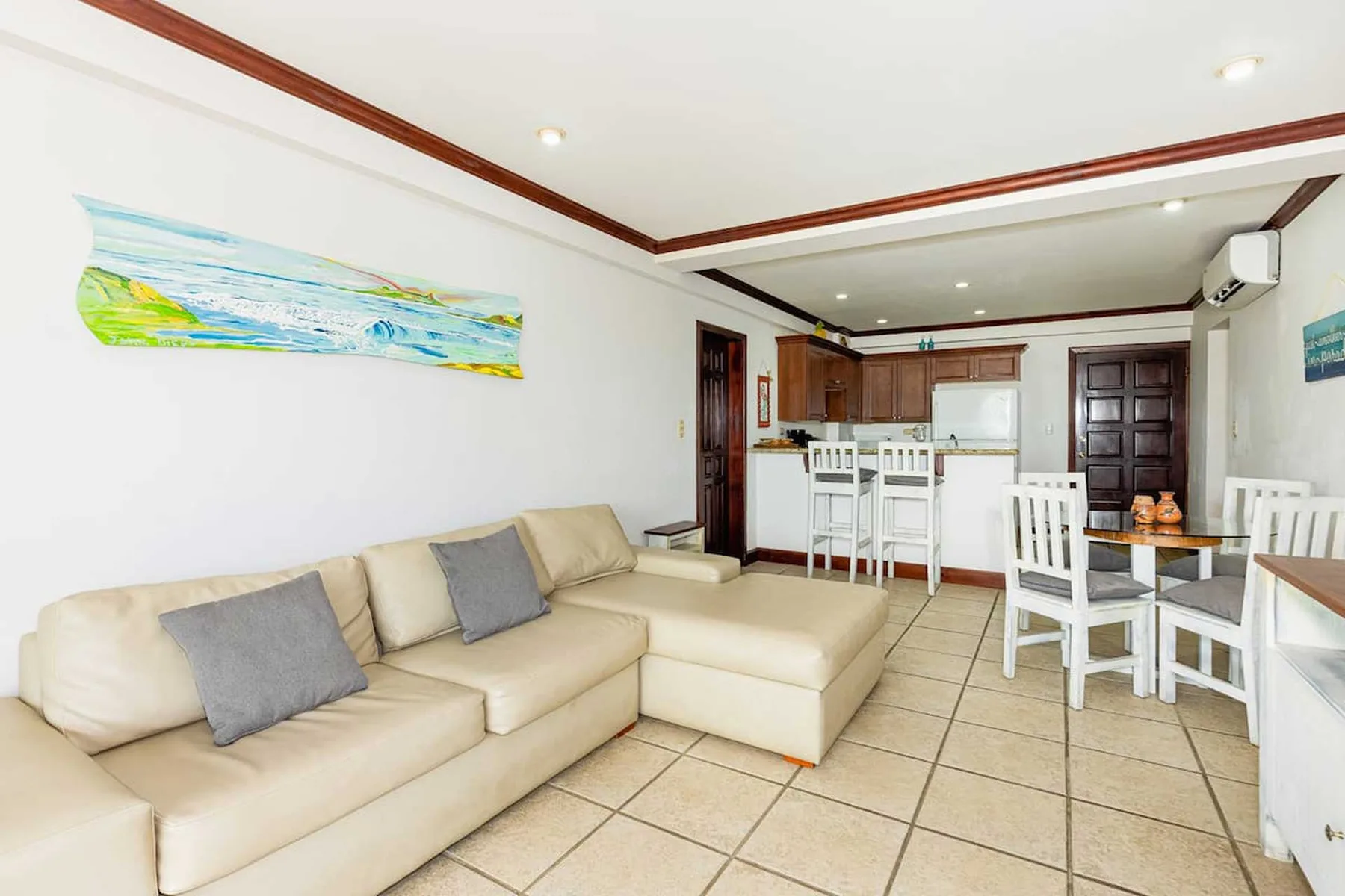 A bright living and dining area with a beige sectional and a white dining table.