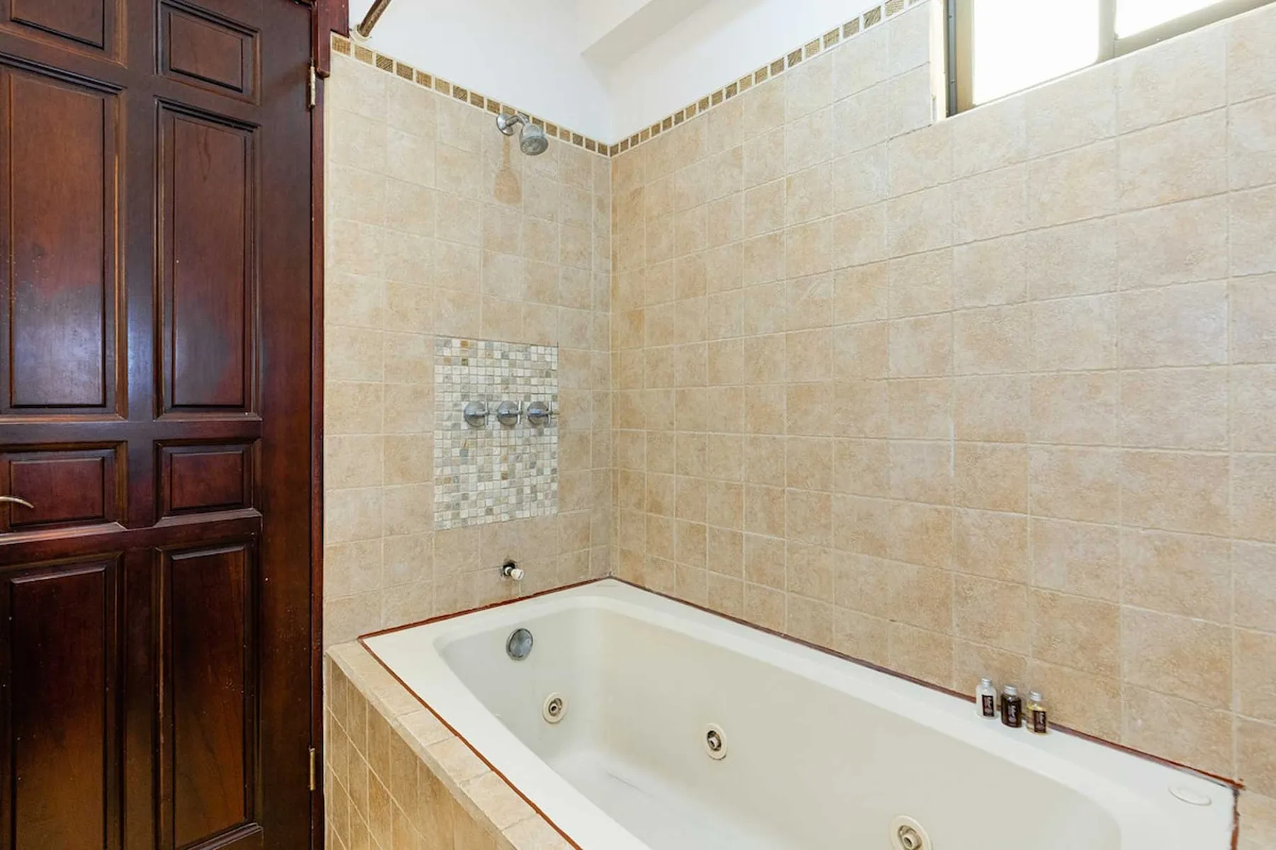 A tiled bathroom features a built-in bathtub beside a dark wooden door.